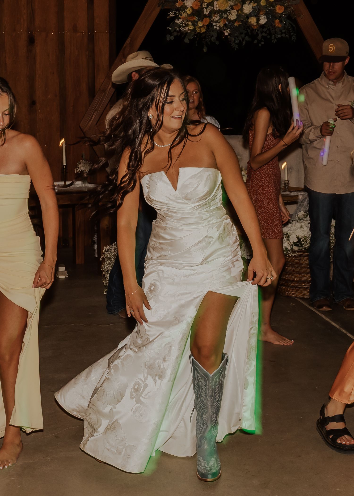 Bride in white dress and turquoise cowboy boots dancing at rustic barn reception.