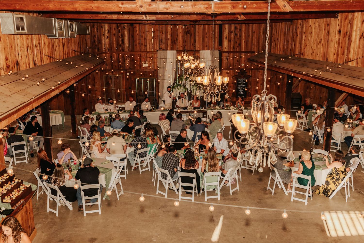 Rustic barn wedding reception setup with string lights and white chairs.