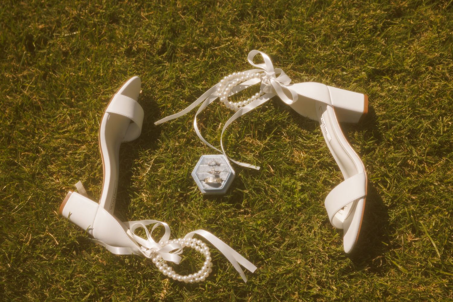 White wedding heels arranged in a circle on grass with delicate lace details.