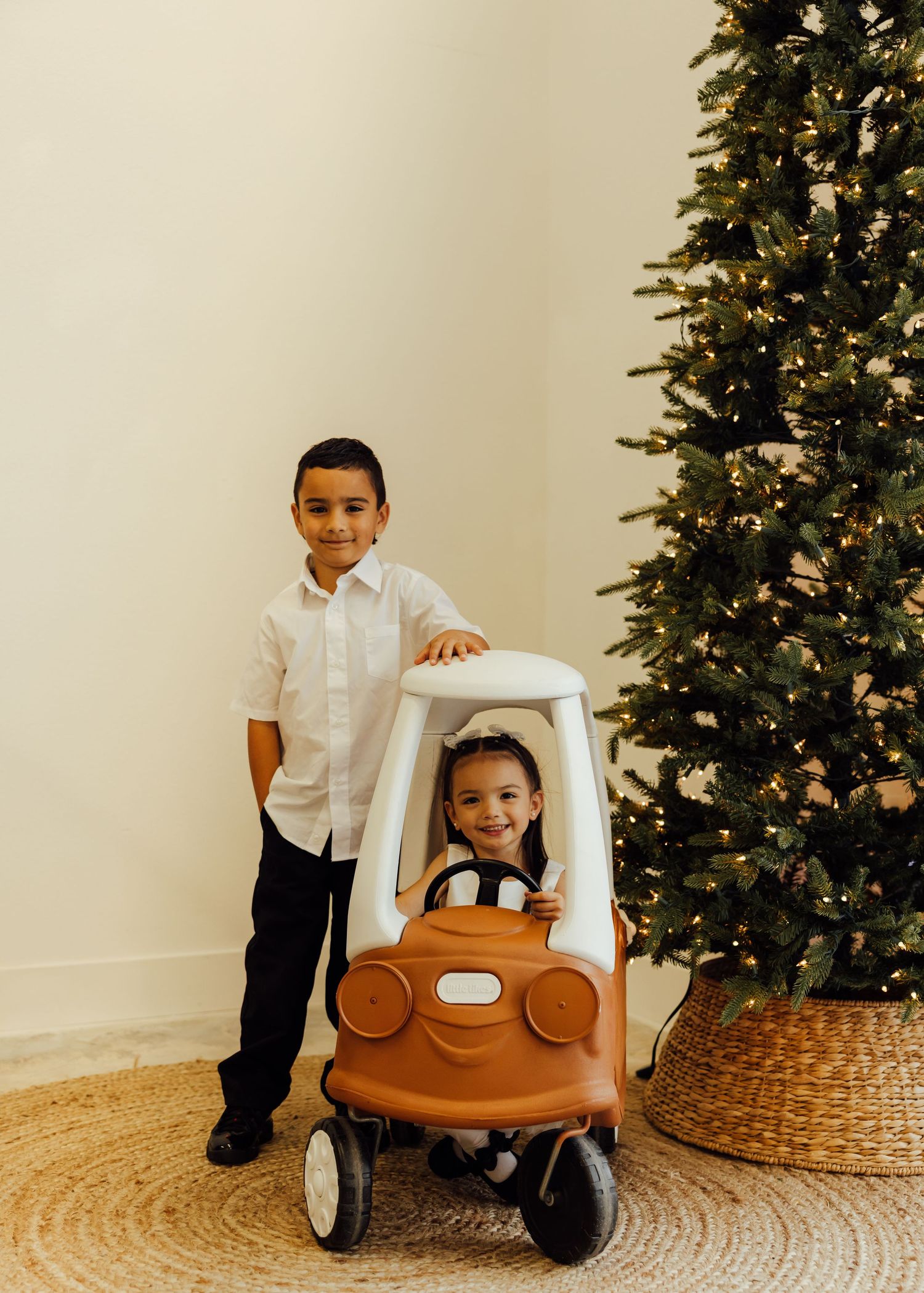 Children playing with a wooden toy car in front of a decorated Christmas tree.