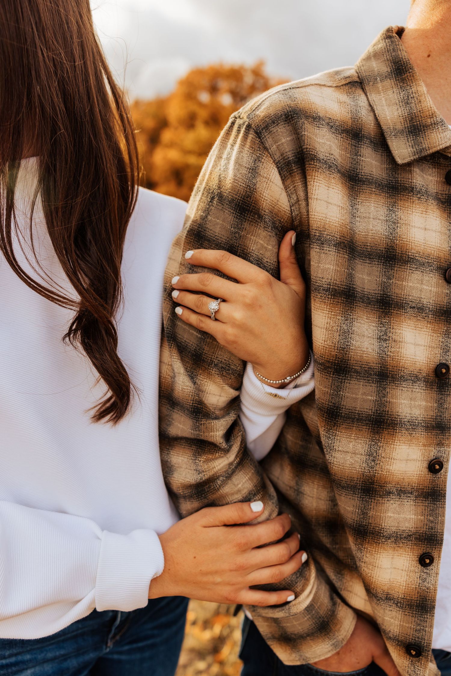 Close-up details of embrace wearing plaid and white during fall engagement photos.