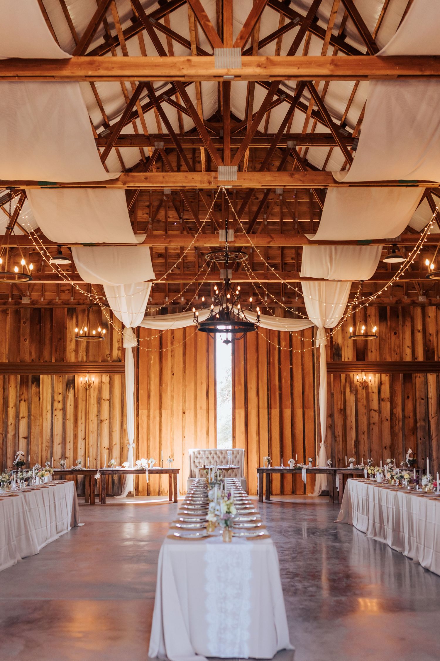 A rustic barn venue with white draping and chandeliers set up for an elegant wedding reception.