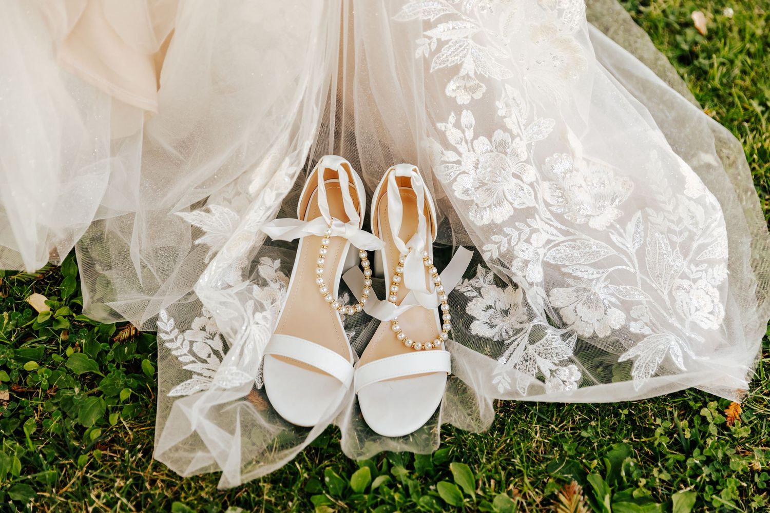 White wedding shoes and lace dress details on grass with delicate styling.
