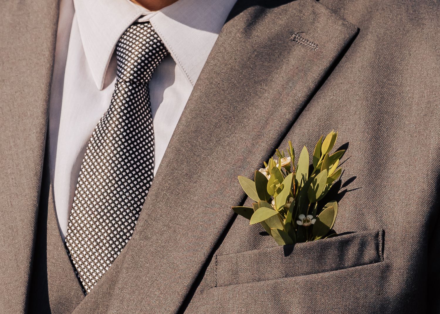 A close-up of a grey suit jacket with polka dot tie and yellow boutonniere.