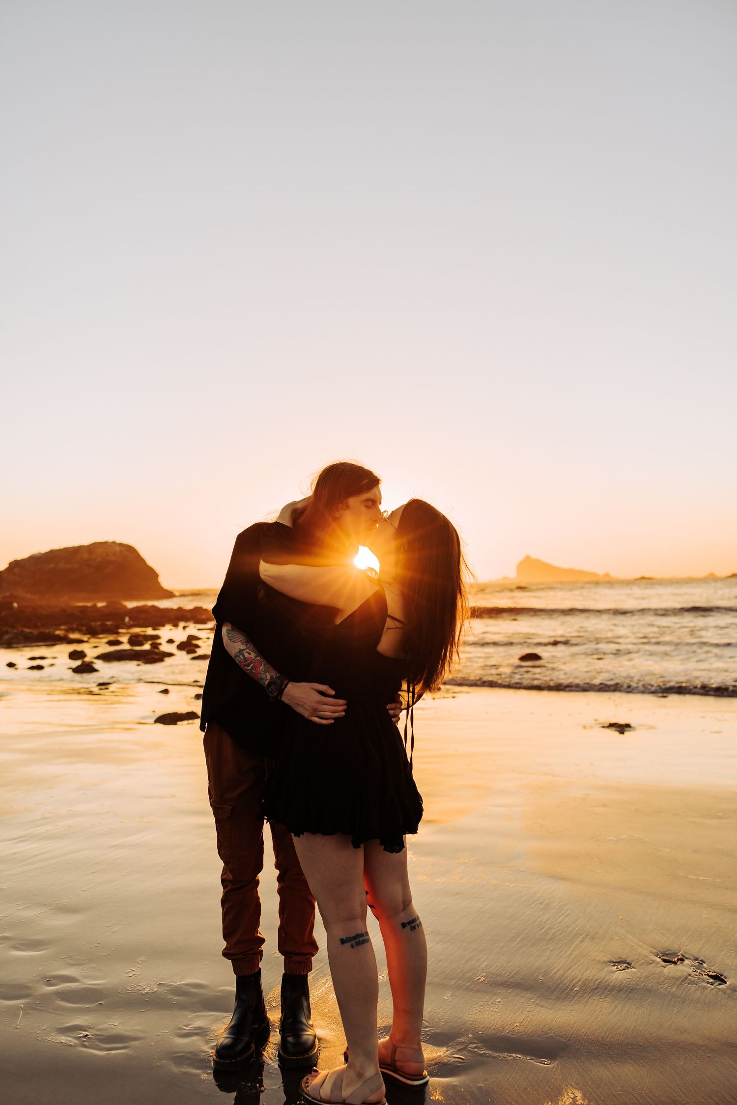 Couple embracing on beach at sunset with sun rays peeking through.