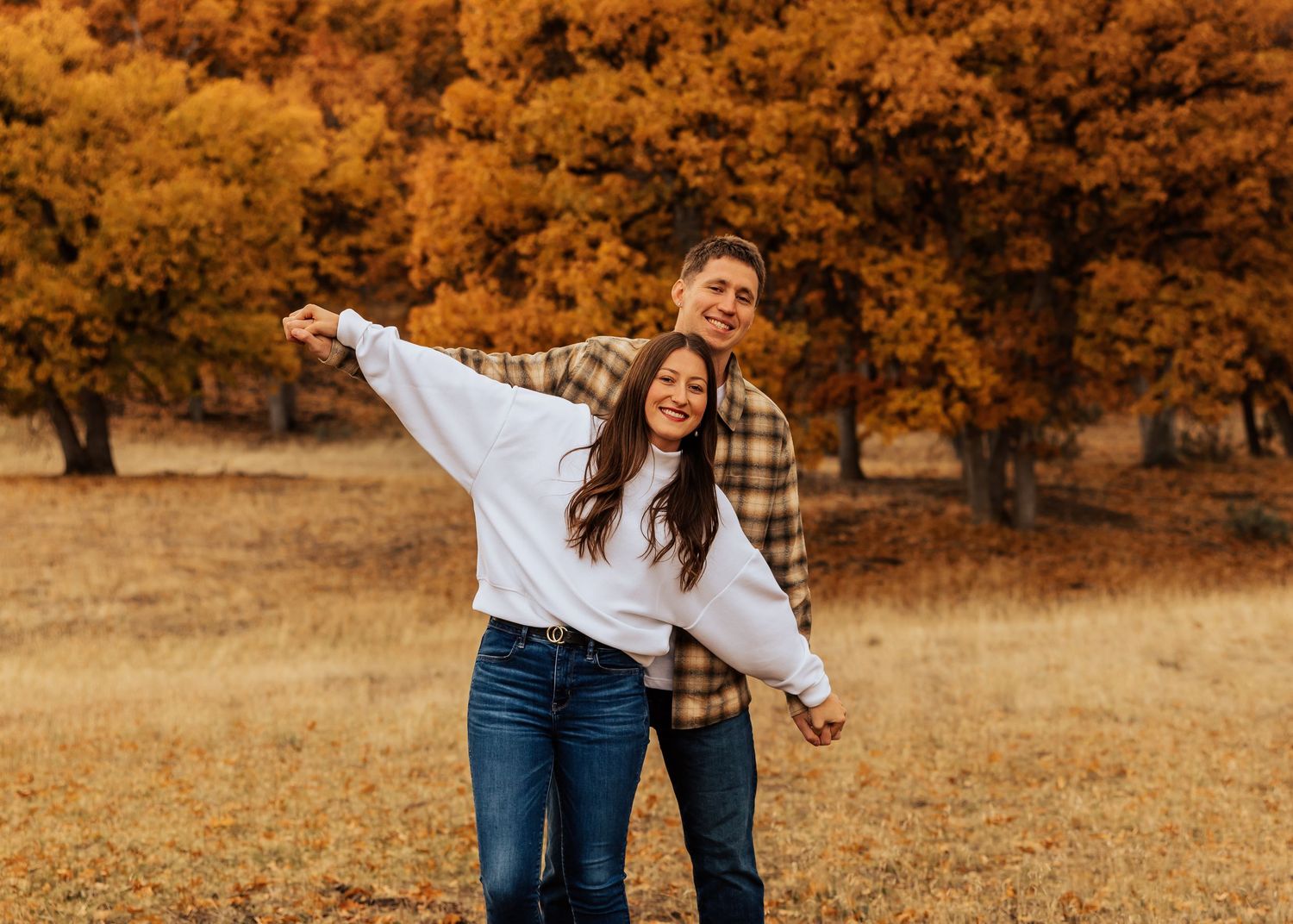Two people share tender moments against a backdrop of warm fall colors and trees.