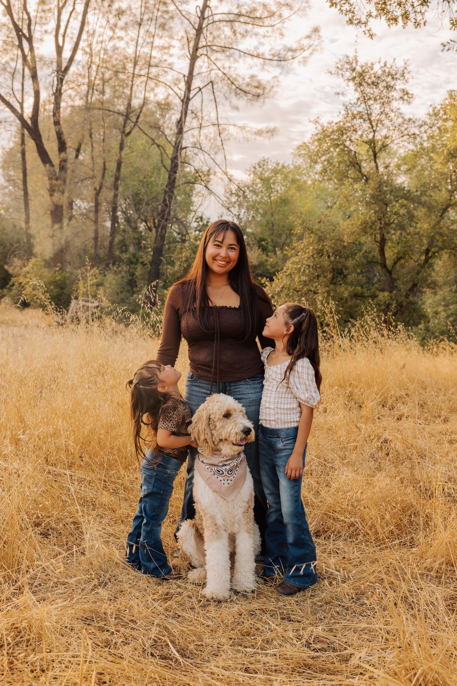 Family posing with their fluffy white dog in a rustic outdoor setting with tall grass.