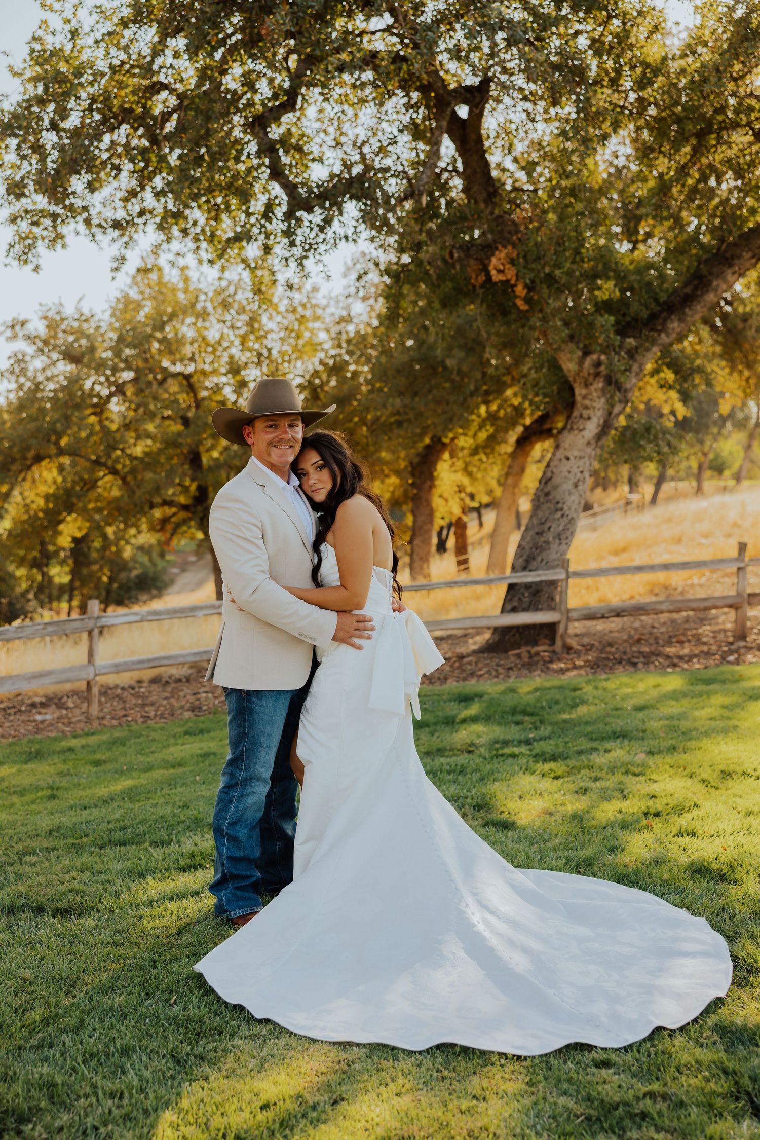 Romantic wedding couple poses on grassy hill during golden hour with flowing white dress.