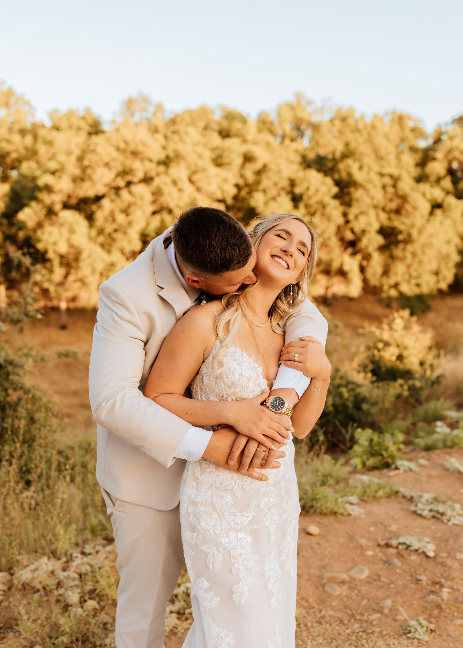 A romantic wedding photoshoot with a couple embracing in golden sunlight by a lake.