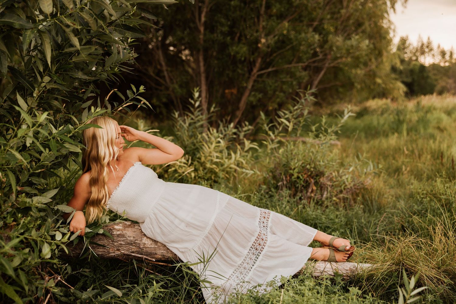 A white sundress flows in the golden sunlight against a lush green field during a summer photoshoot.