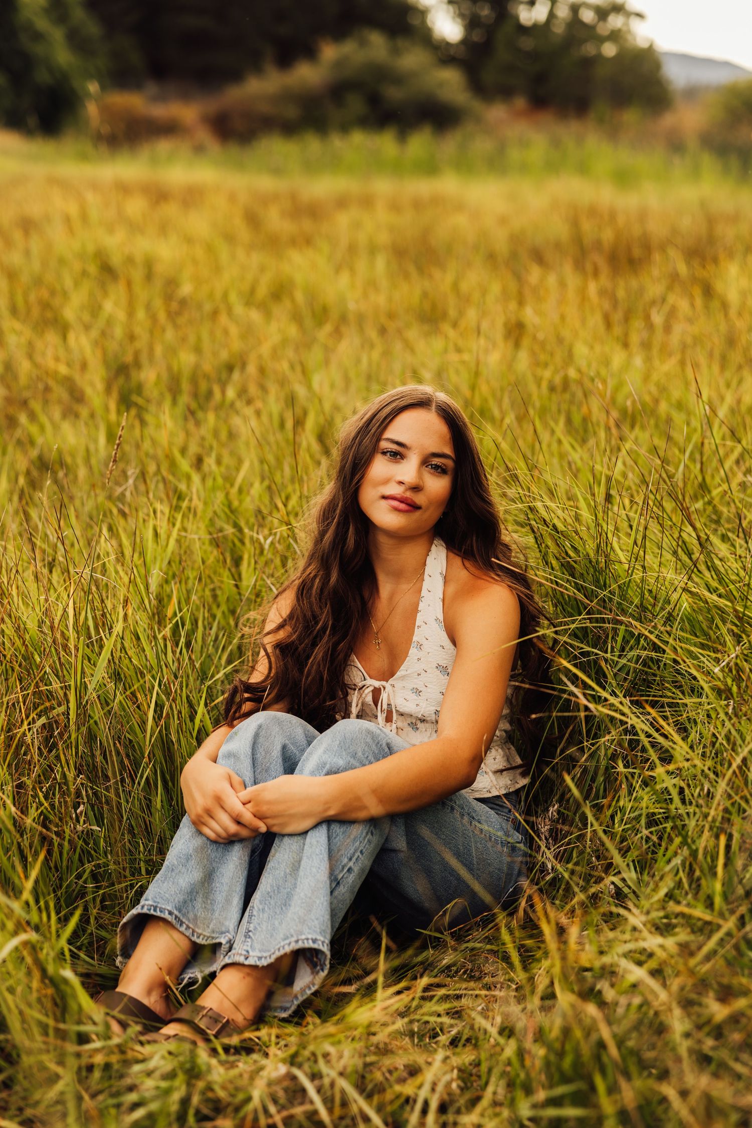 A person in denim and white top relaxes in tall grass during golden hour.