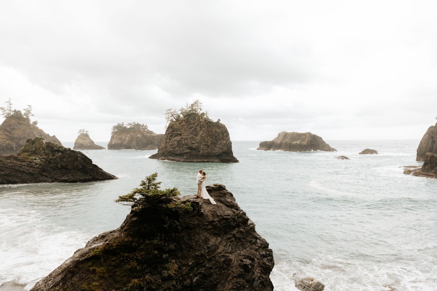 Rugged coastal rock formations and sea stacks rise from the misty Pacific Ocean along a dramatic shoreline.