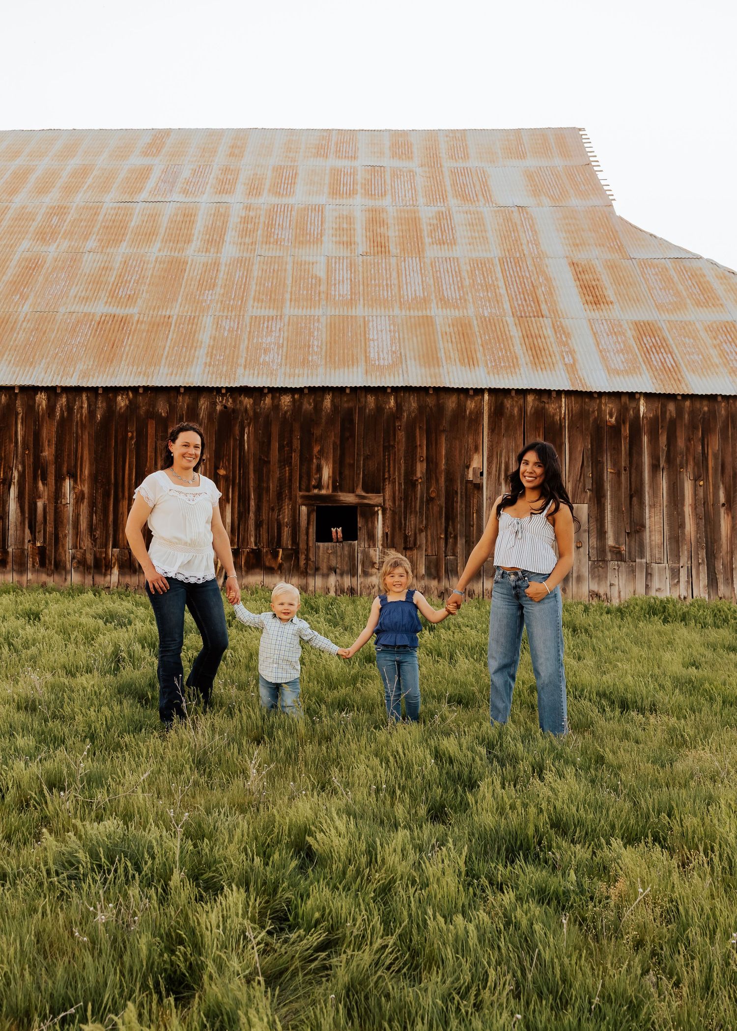 Family photo session in front of rustic barn with green grass and natural lighting.