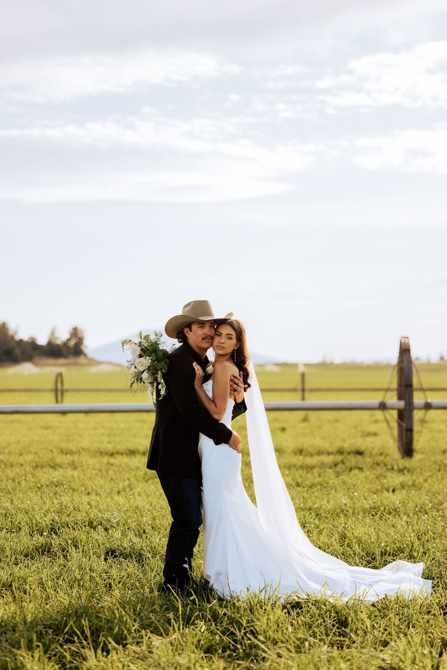 Newlyweds share an intimate moment in a sunlit meadow with a flowing white wedding dress.