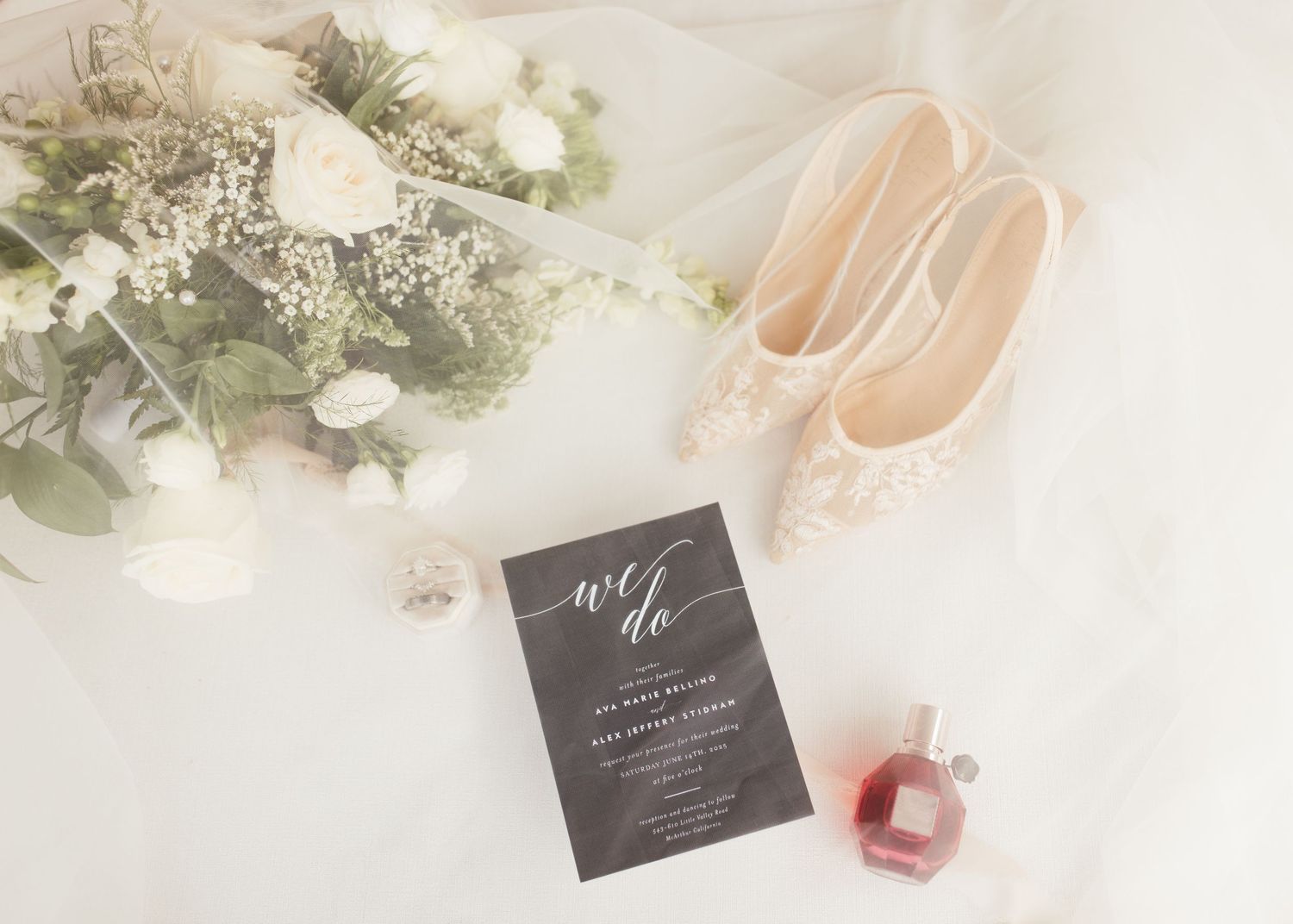 Elegant wedding details including flowers, invitation and pink accessories on white surface.