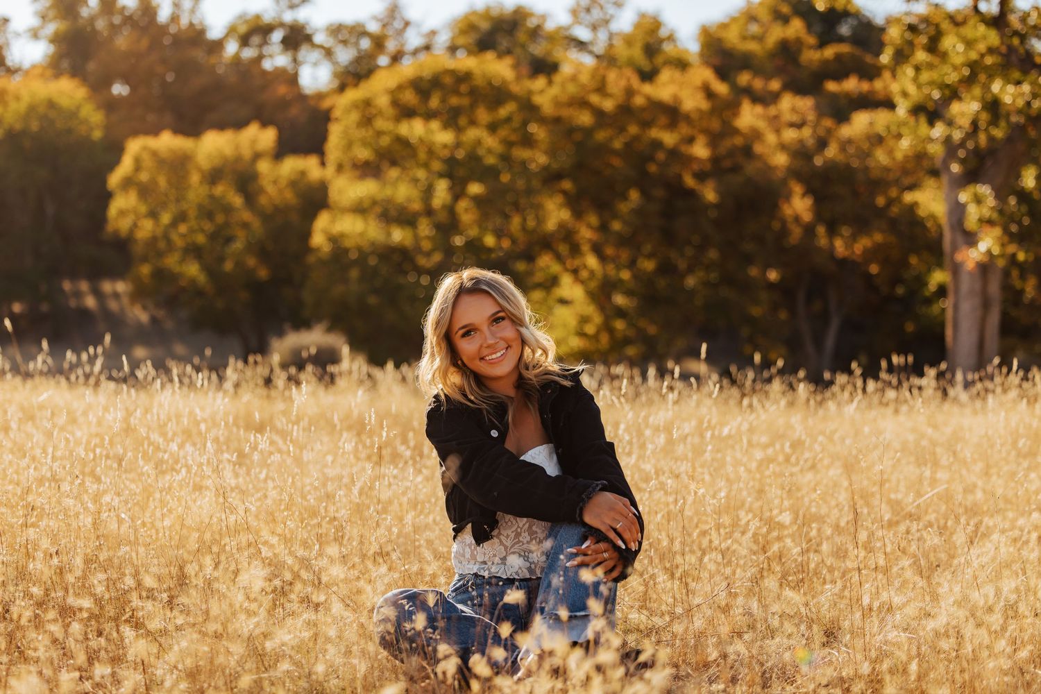 Outdoor portrait session in a sun-lit meadow with autumn trees in the background.