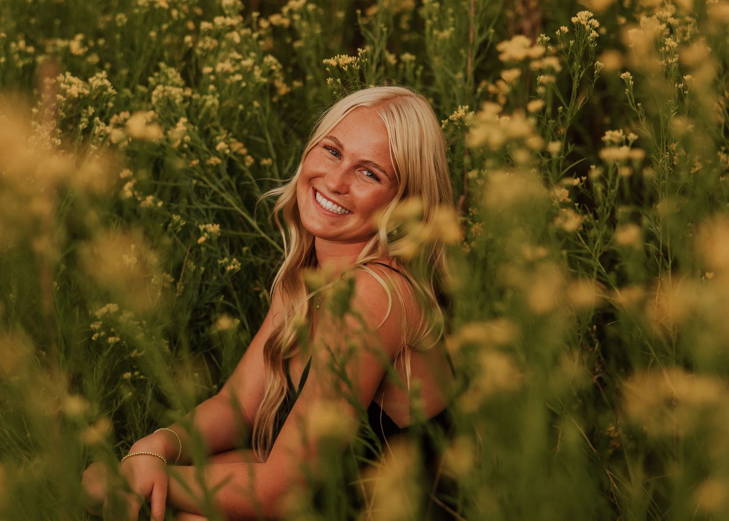 Artistic portrait through yellow wildflowers during golden hour in a meadow.