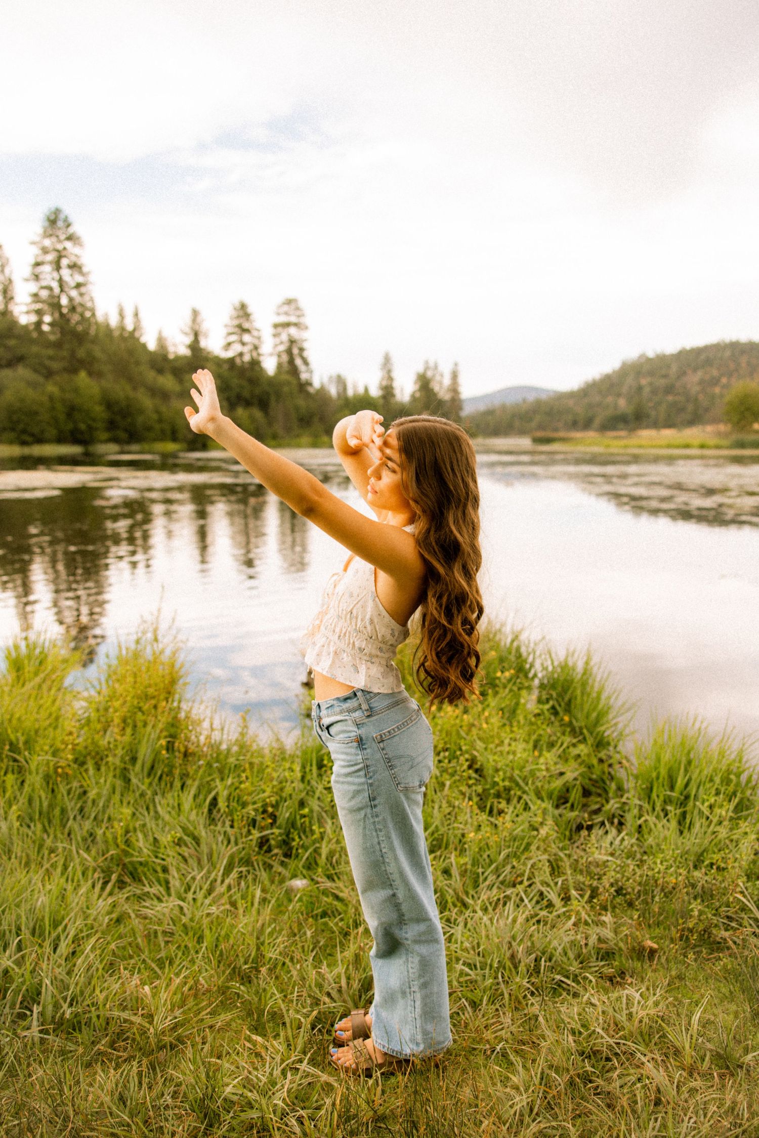 A golden hour photoshoot by a serene lake with tall grass and mountains in the background.