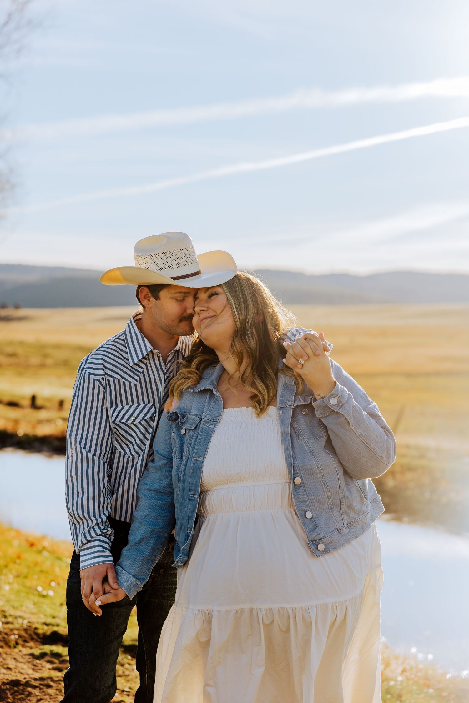 A tender moment between couple in western wear with scenic ranch landscape behind them.