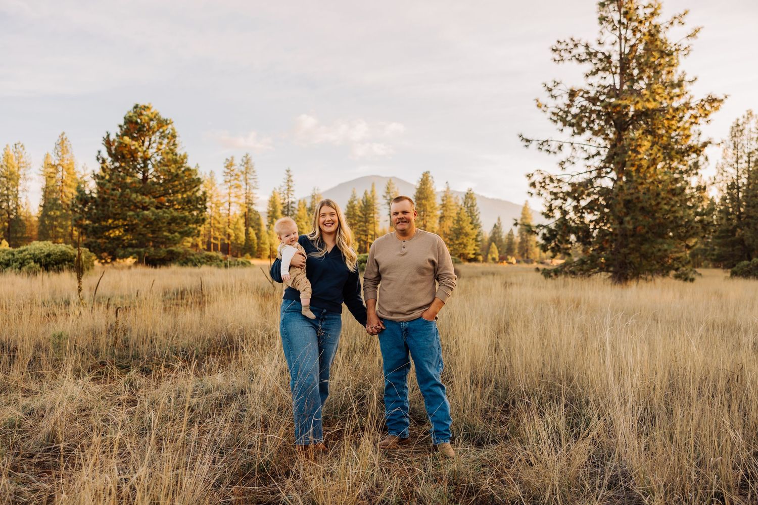 A family stands together in a scenic mountain meadow during golden hour.
