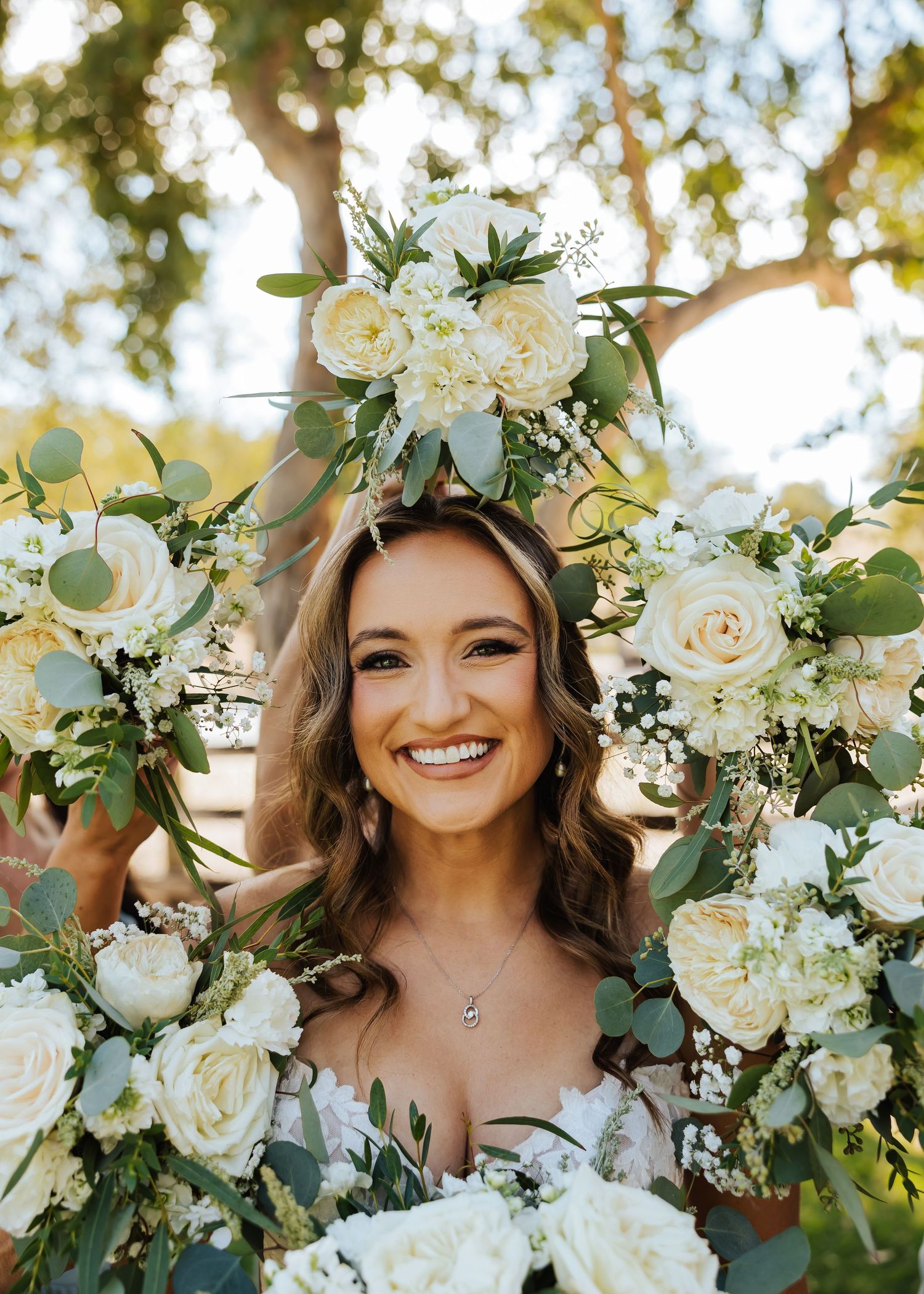 Smiling bride framed by white rose and eucalyptus floral arch on her wedding day.