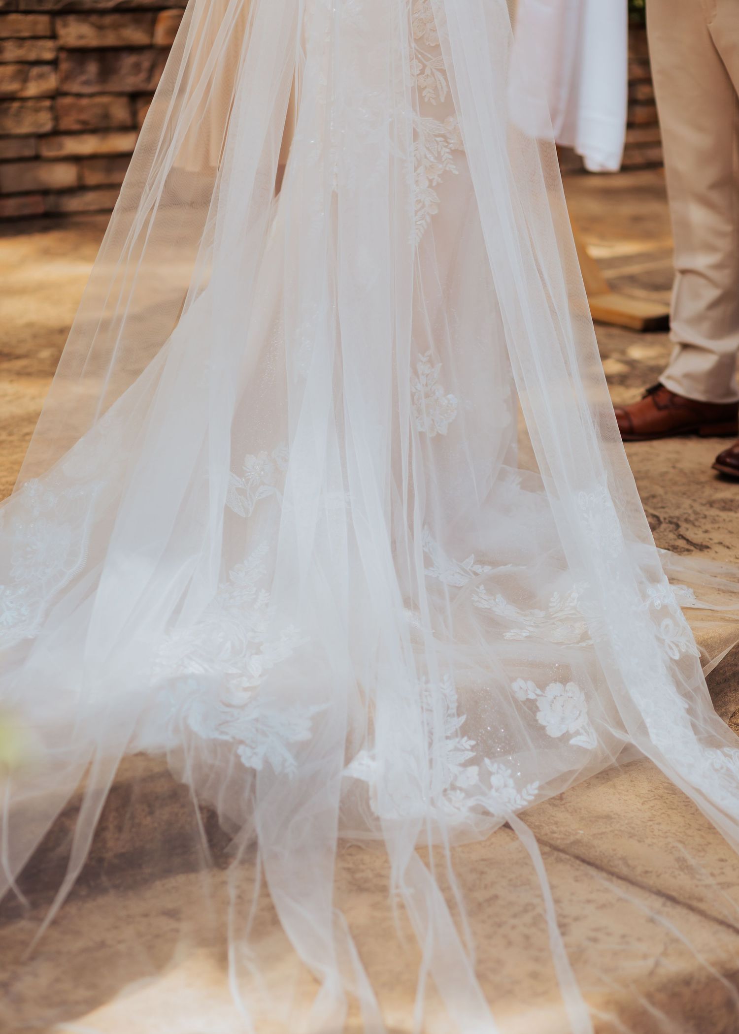Detailed view of a flowing wedding dress train with delicate lace appliques on stone steps.