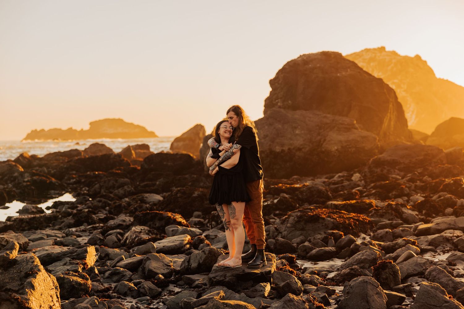 Romantic moment on rocky coastline during golden hour with dramatic cliffs and ocean view.