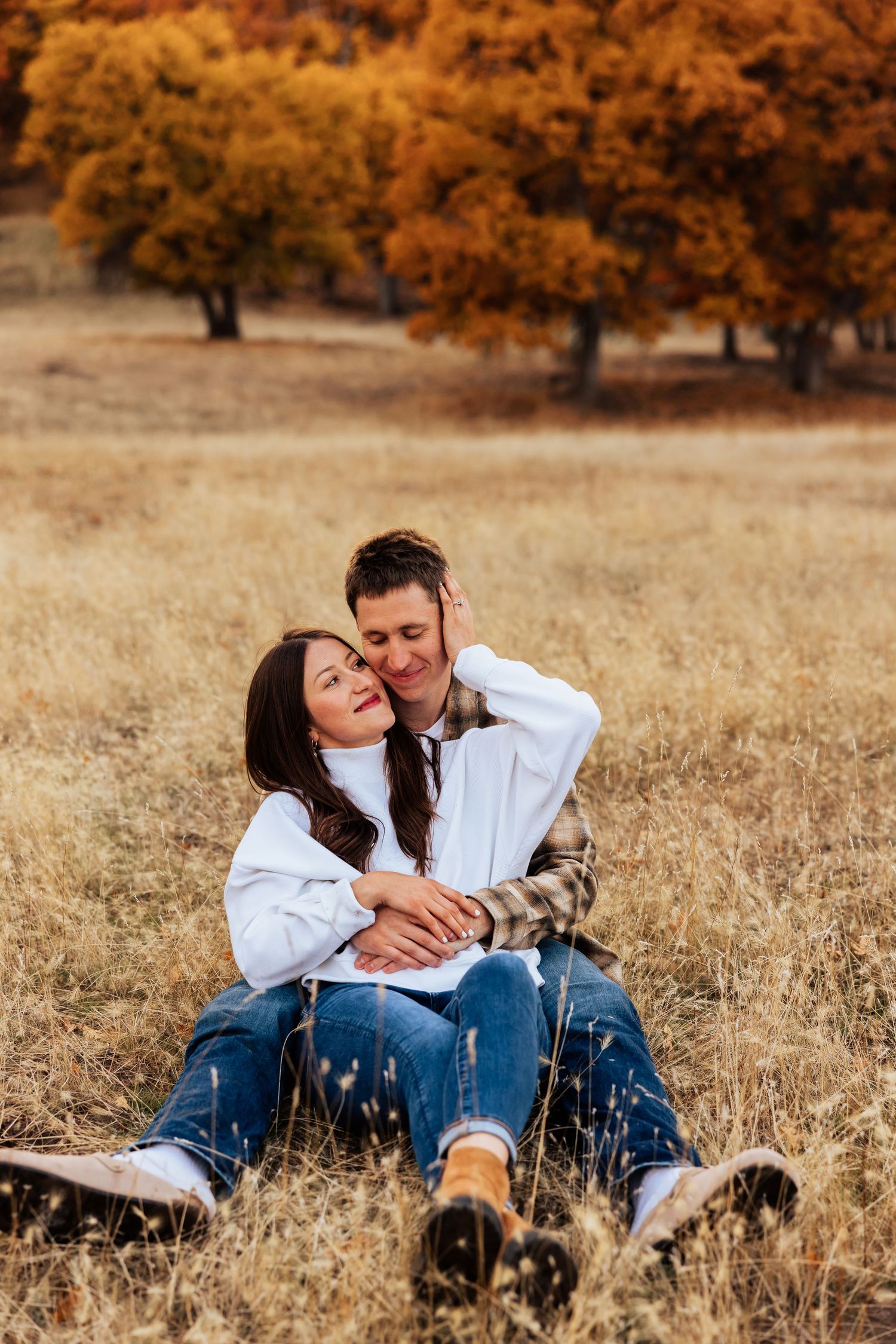 Intimate couple moment captured in a field with fall foliage in the background.