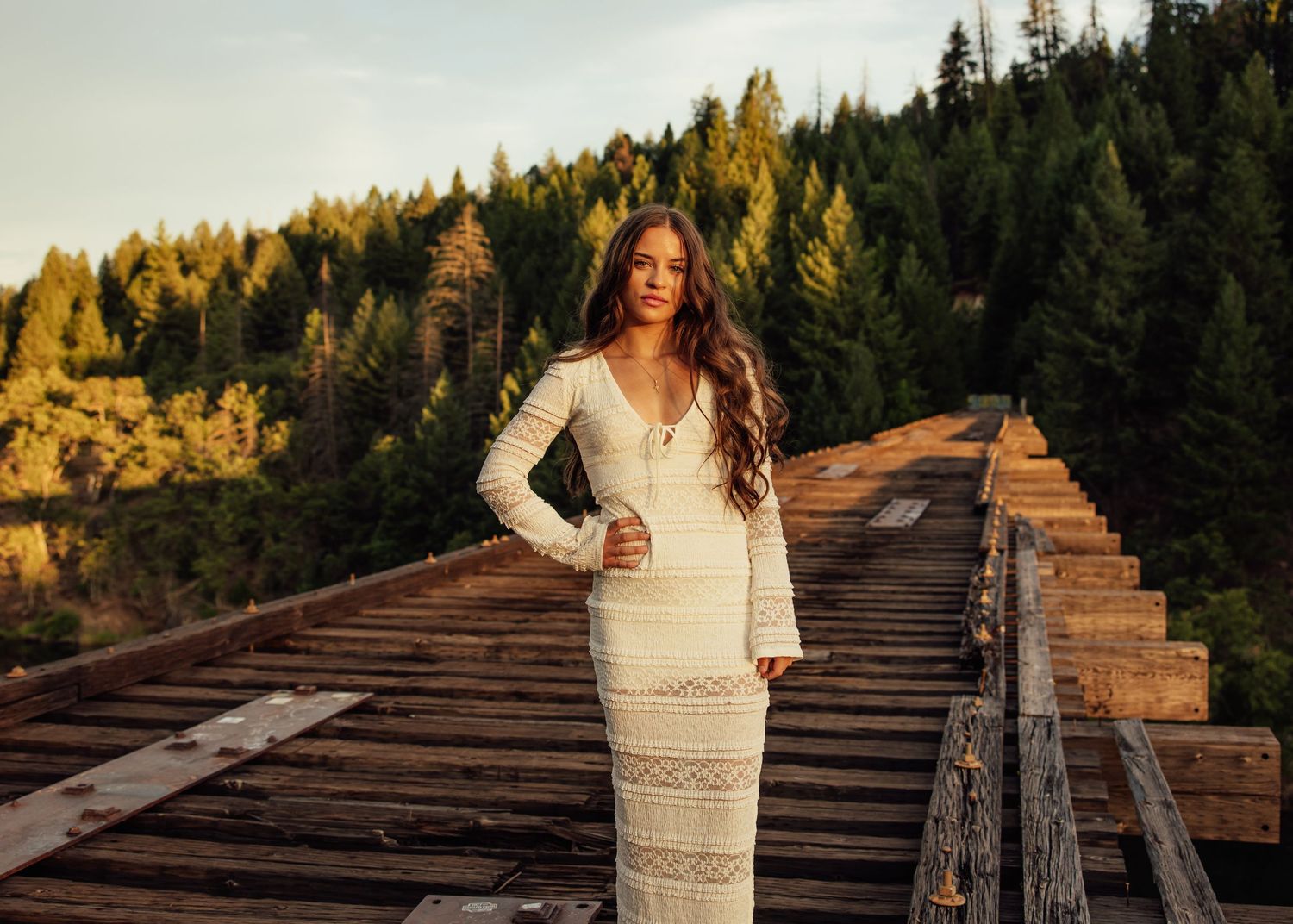 Romantic sunset portrait on rustic wooden railroad tracks surrounded by pine trees.