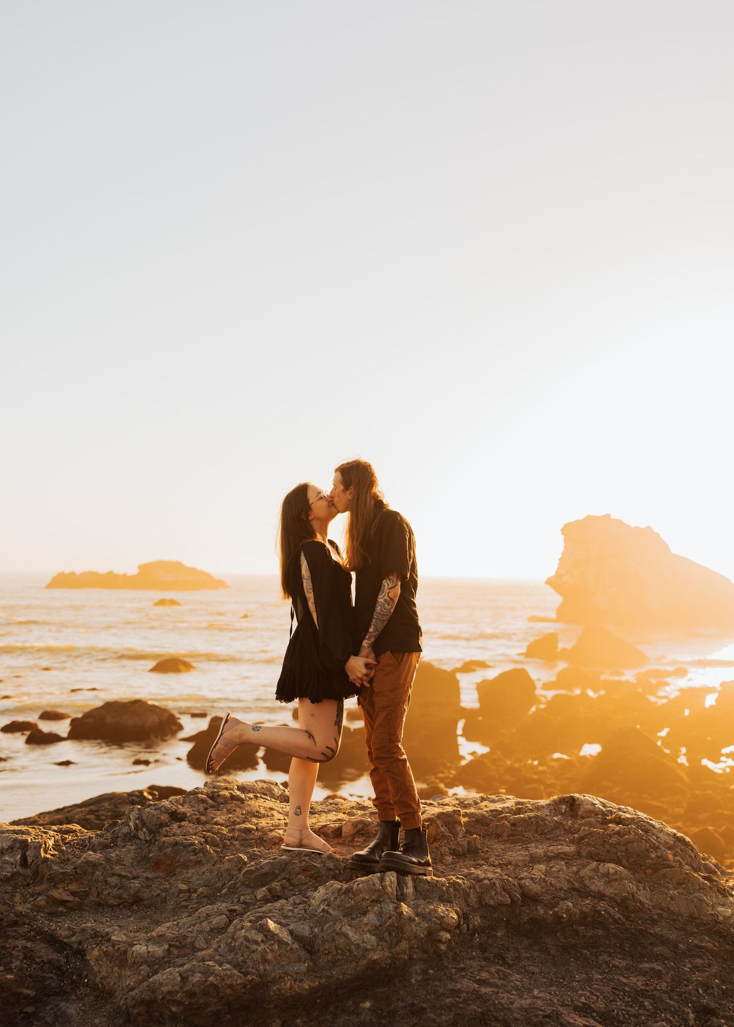 A couple shares a tender moment on coastal rocks during golden hour.