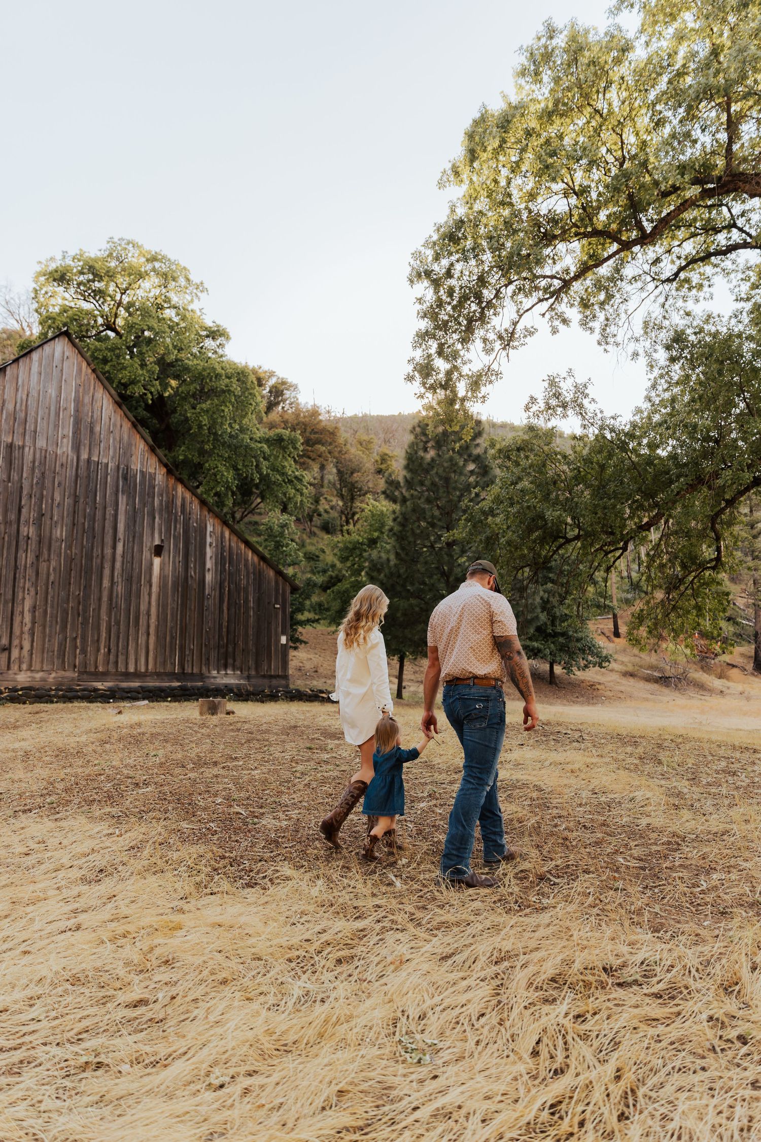 A family walks together across a dry grass field towards a vintage wooden barn.