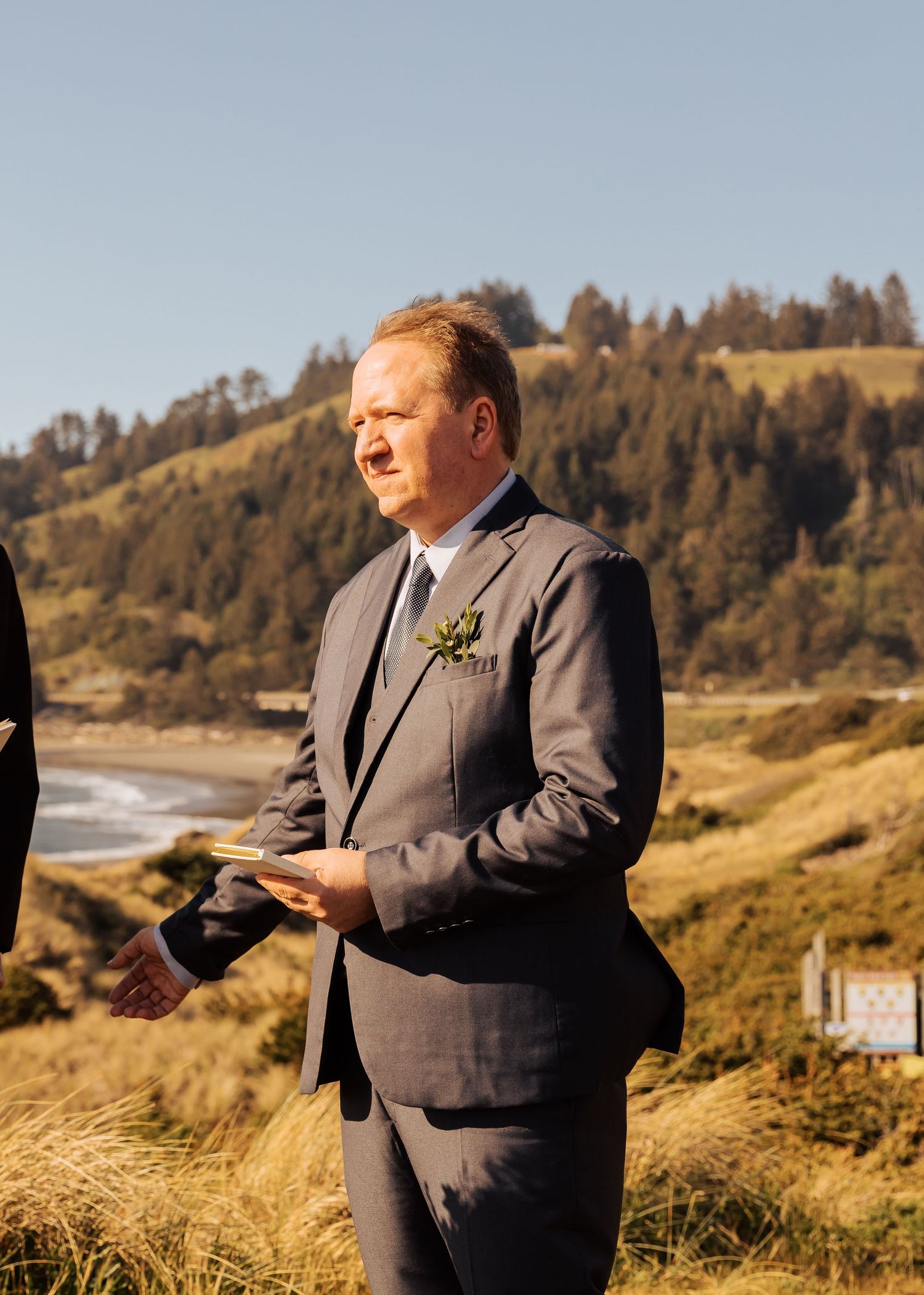 An officiant stands on a rugged coastal path preparing to perform a ceremony.