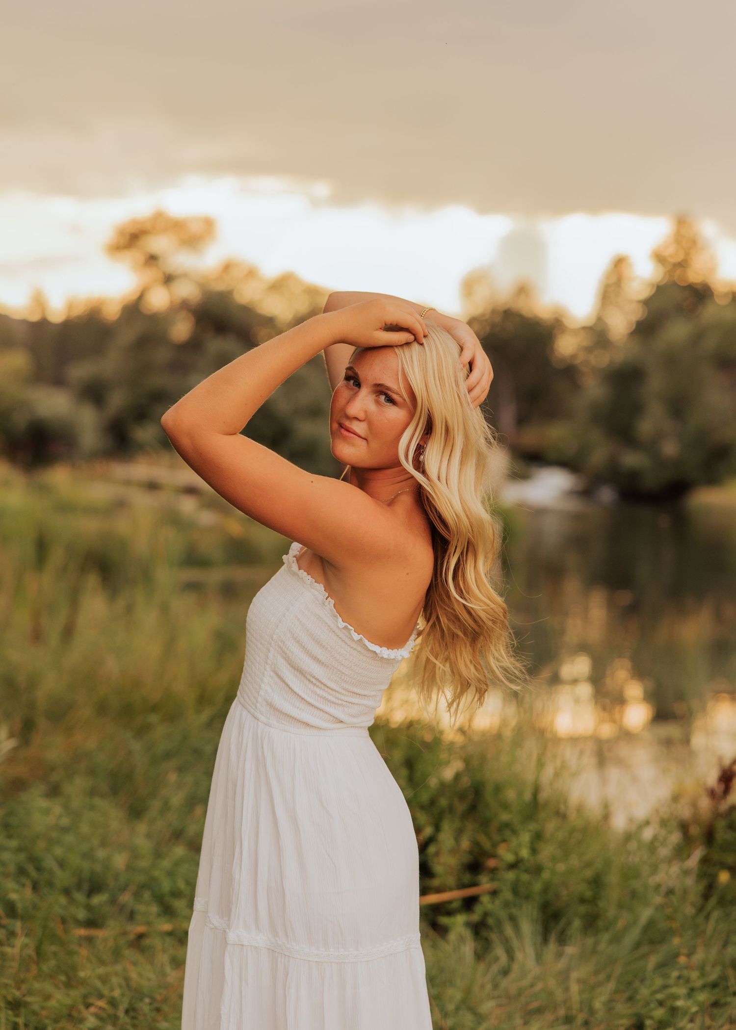 Person in white sundress poses against sunset lake backdrop.