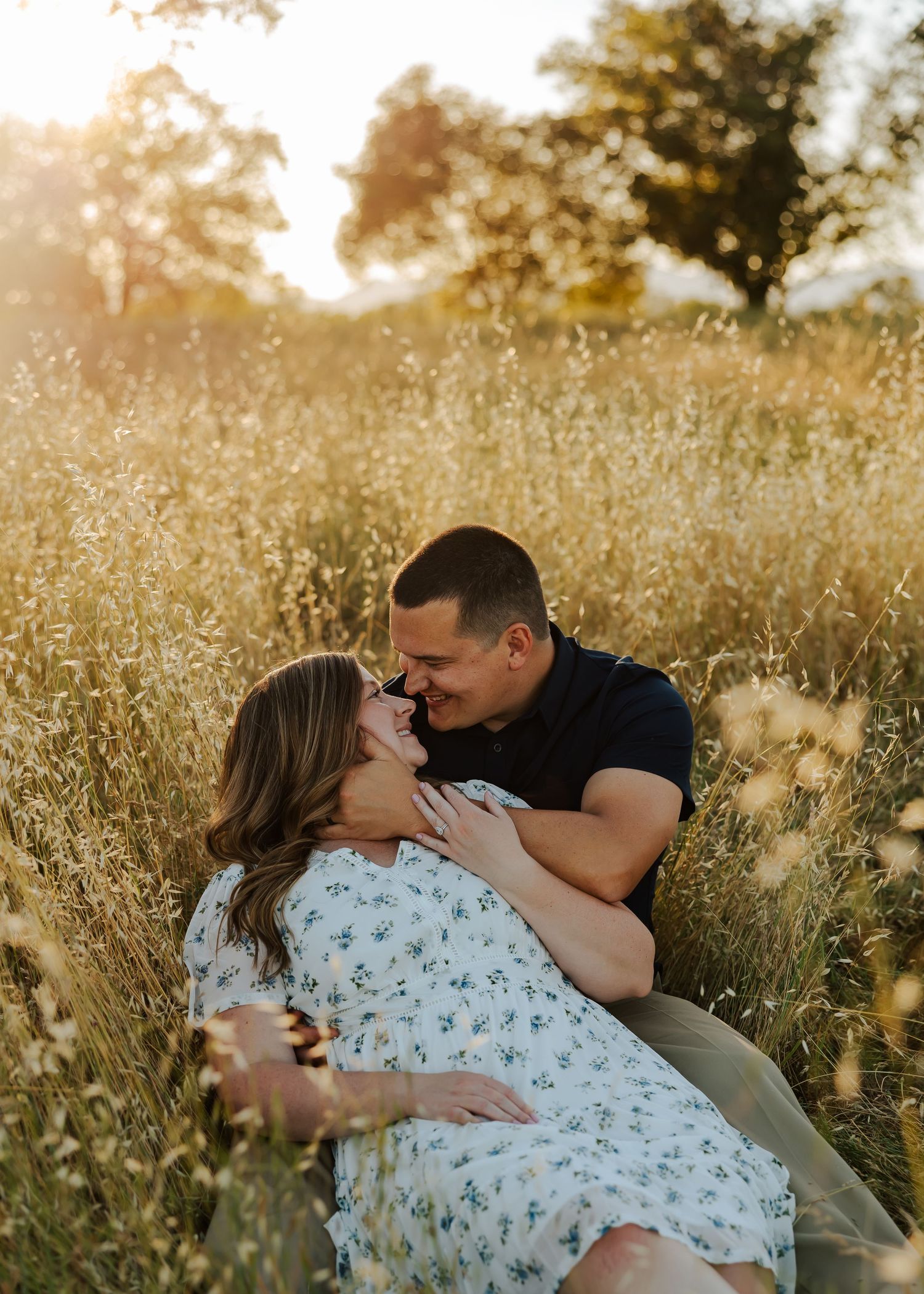 Couple sharing a romantic moment in a golden sunlit field during a maternity photo session at sunset.
