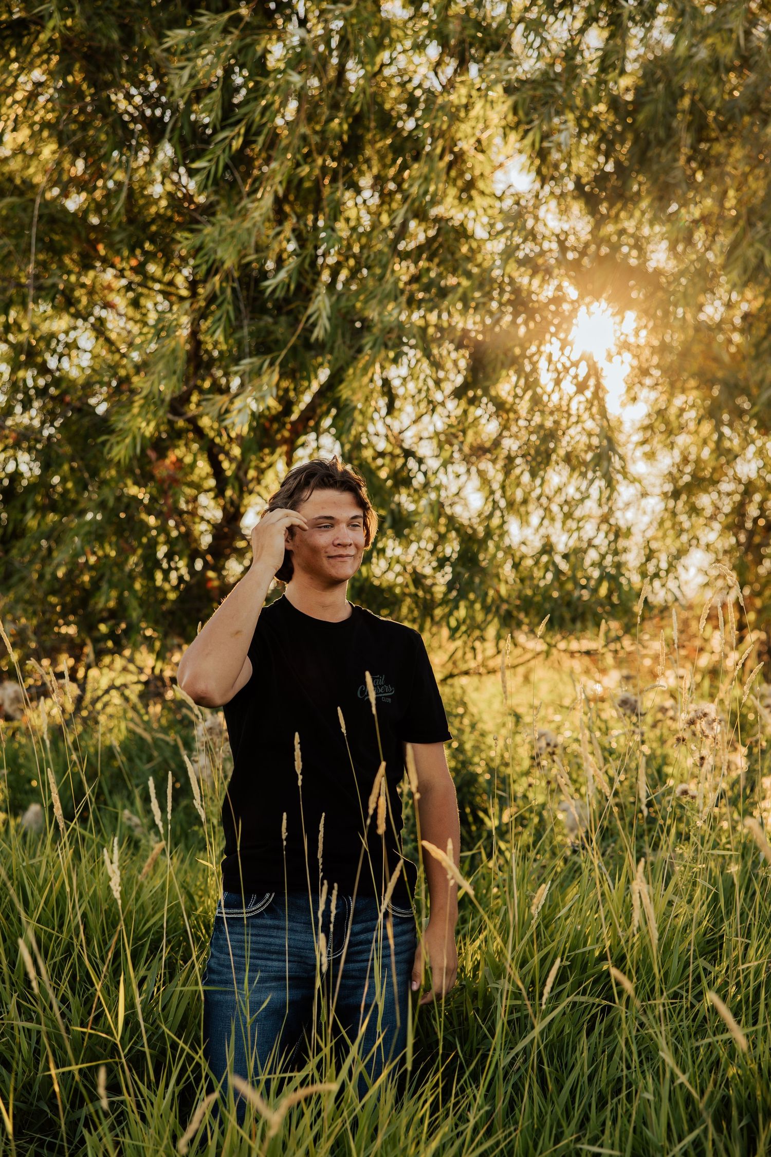 A figure stands among tall grass with sunlight filtering through trees in the background.