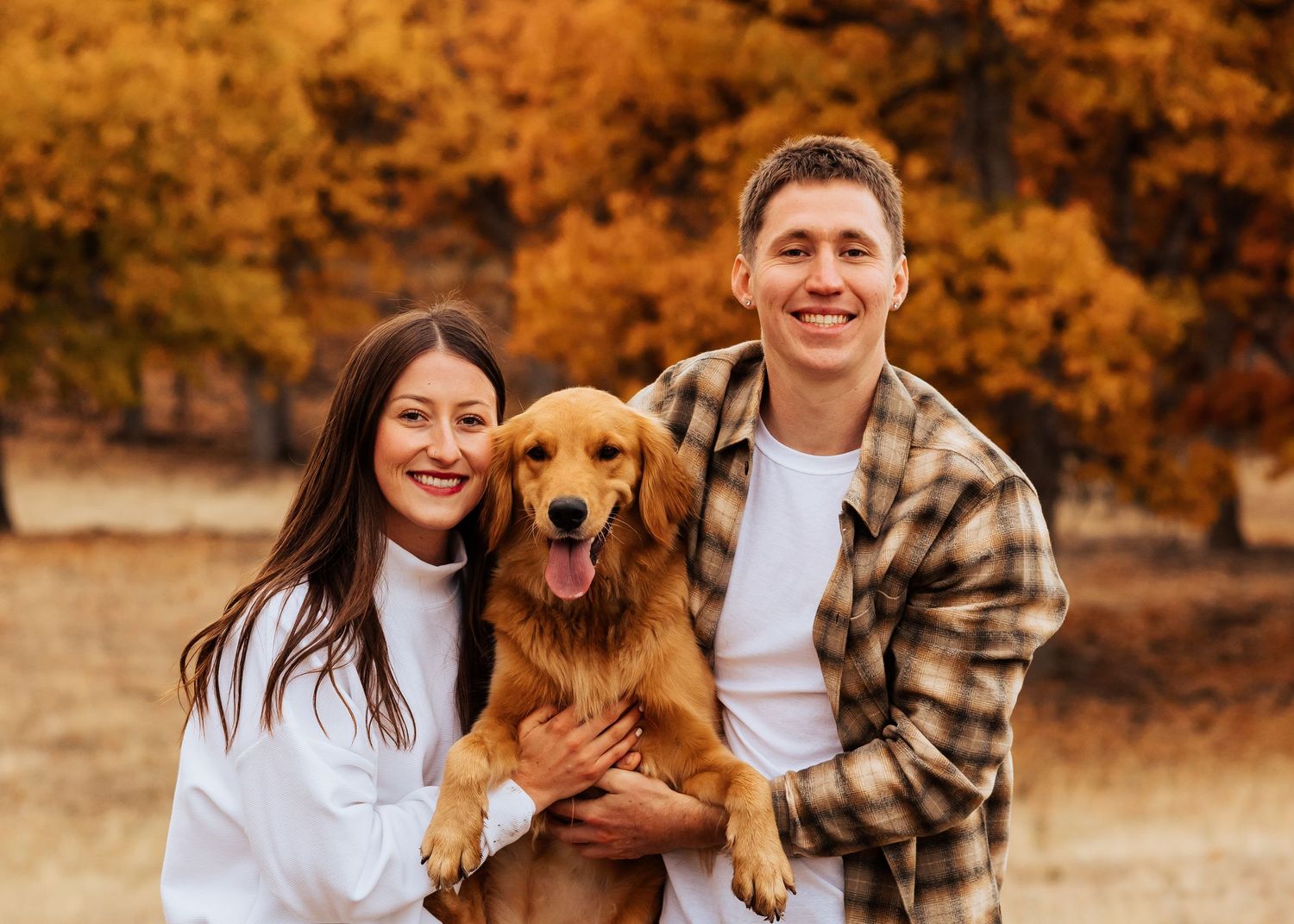 Happy golden retriever with owners in casual attire during autumn photoshoot.