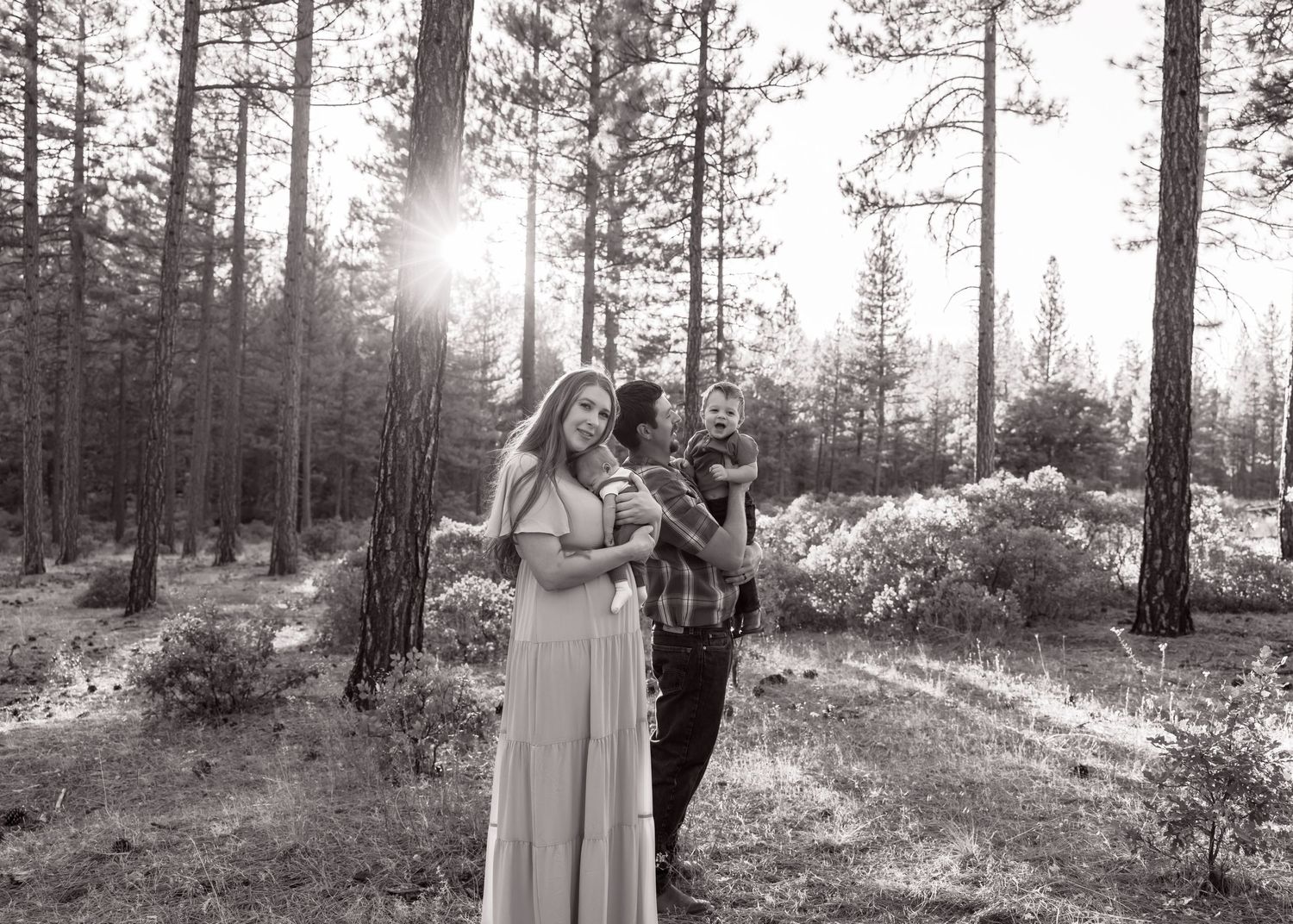Black and white photo of a couple sharing a joyful moment in a sunlit forest.