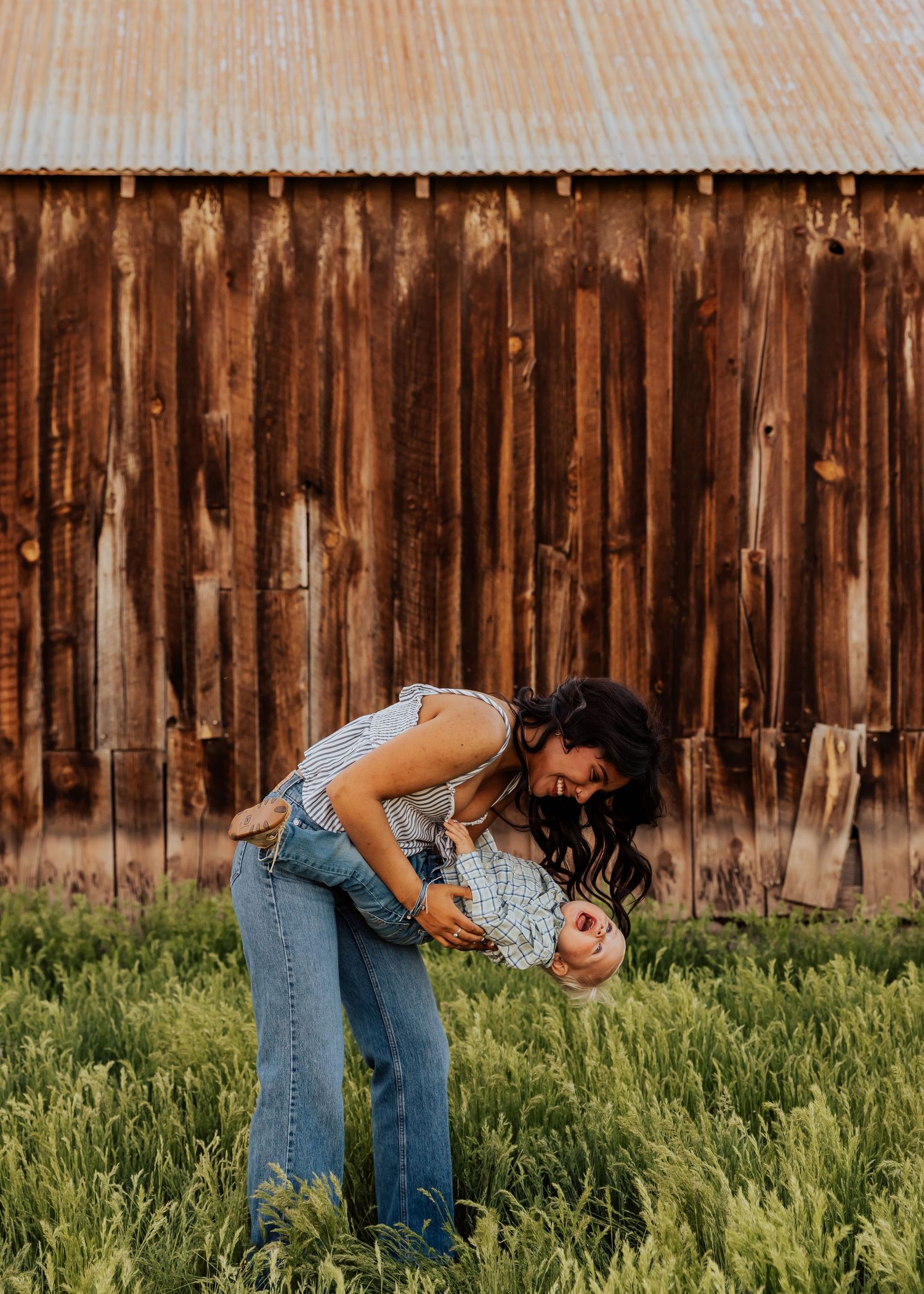 Two people in casual wear embrace near weathered wooden barn wall and tall grass.