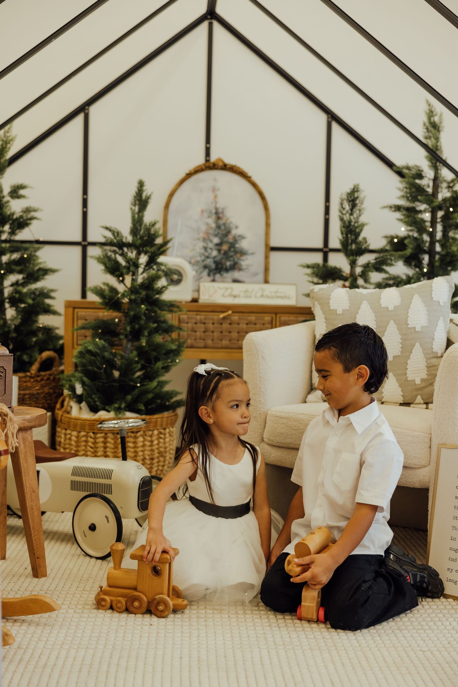Children playing on a white carpeted floor with wooden toys near a Christmas tree.