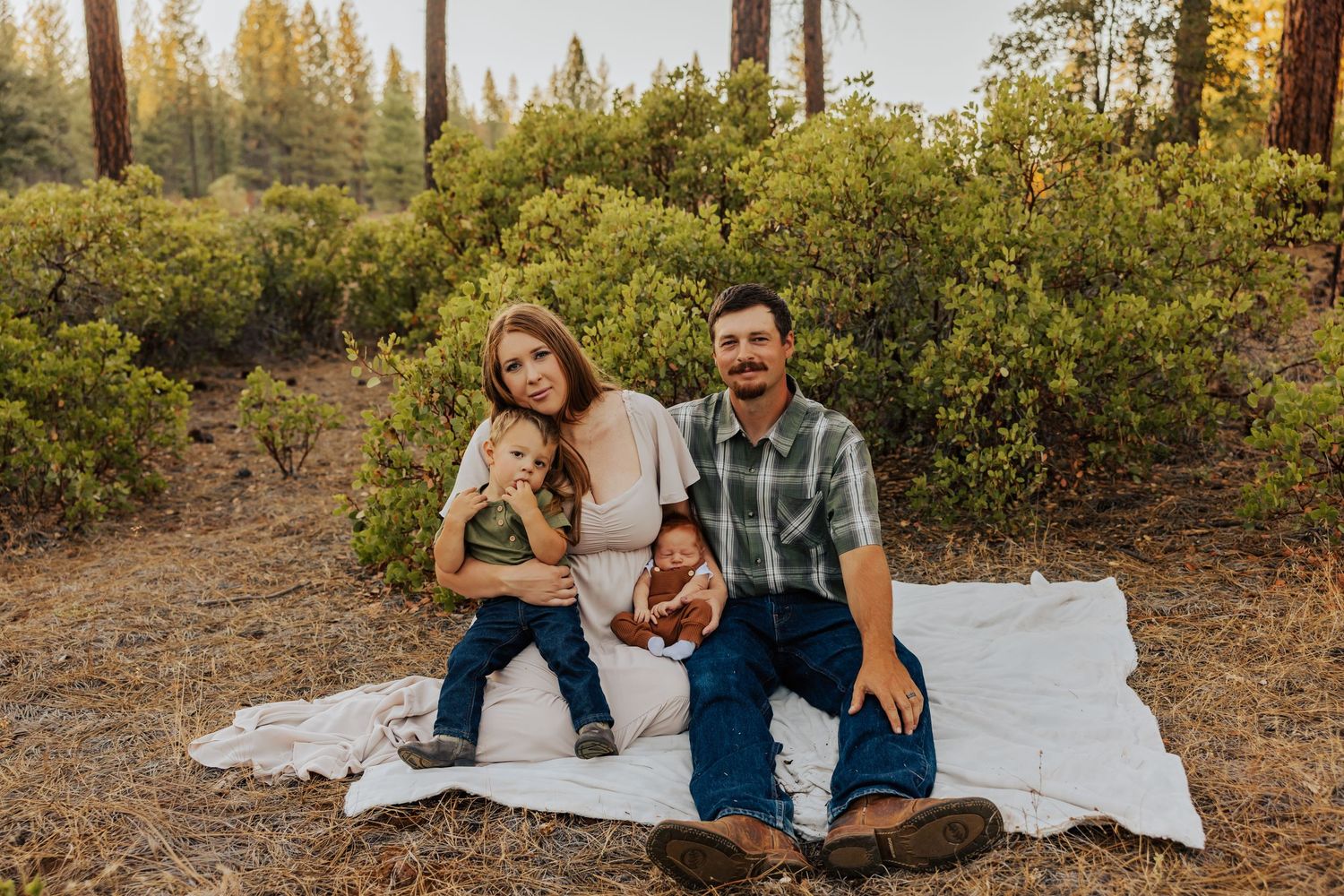 Family spending quality time together on white blanket in forest during sunset.