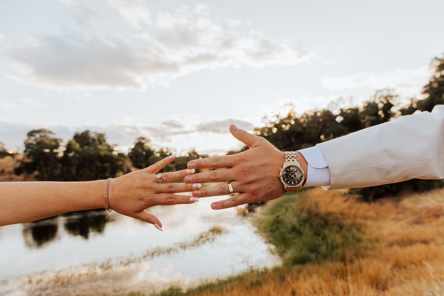 Hands reaching towards each other against a sunset landscape backdrop.
