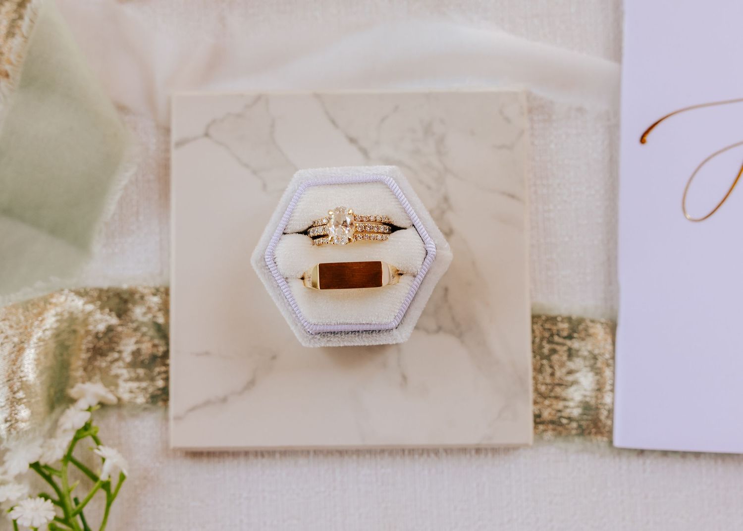 Wedding rings and delicate stationery arranged on white surface with floral details.
