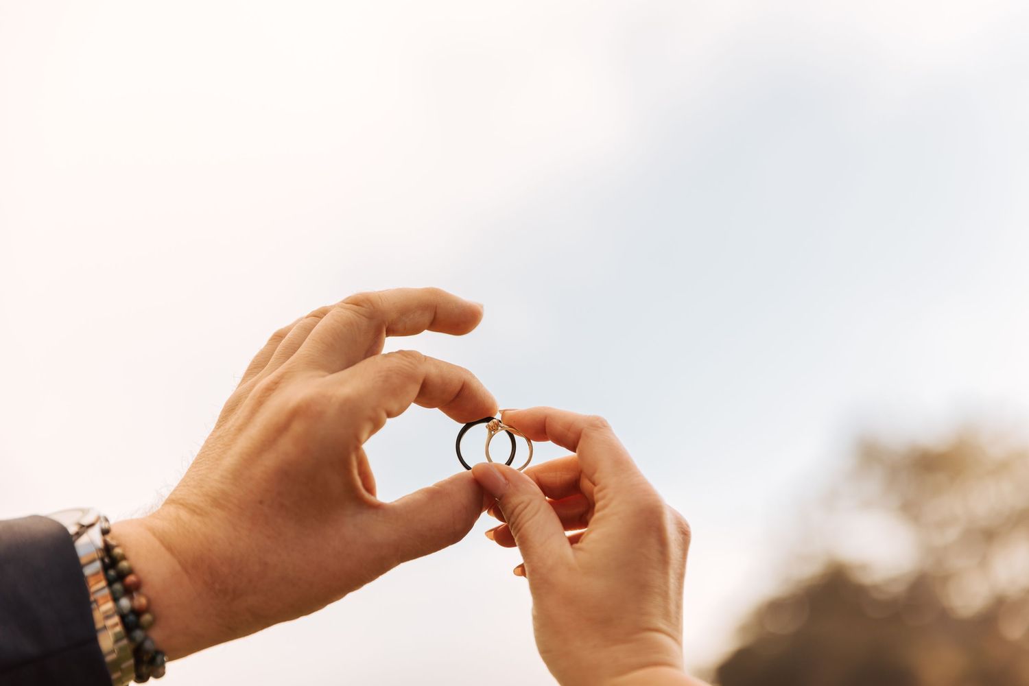 Hands exchanging rings during an outdoor wedding ceremony with soft lighting.