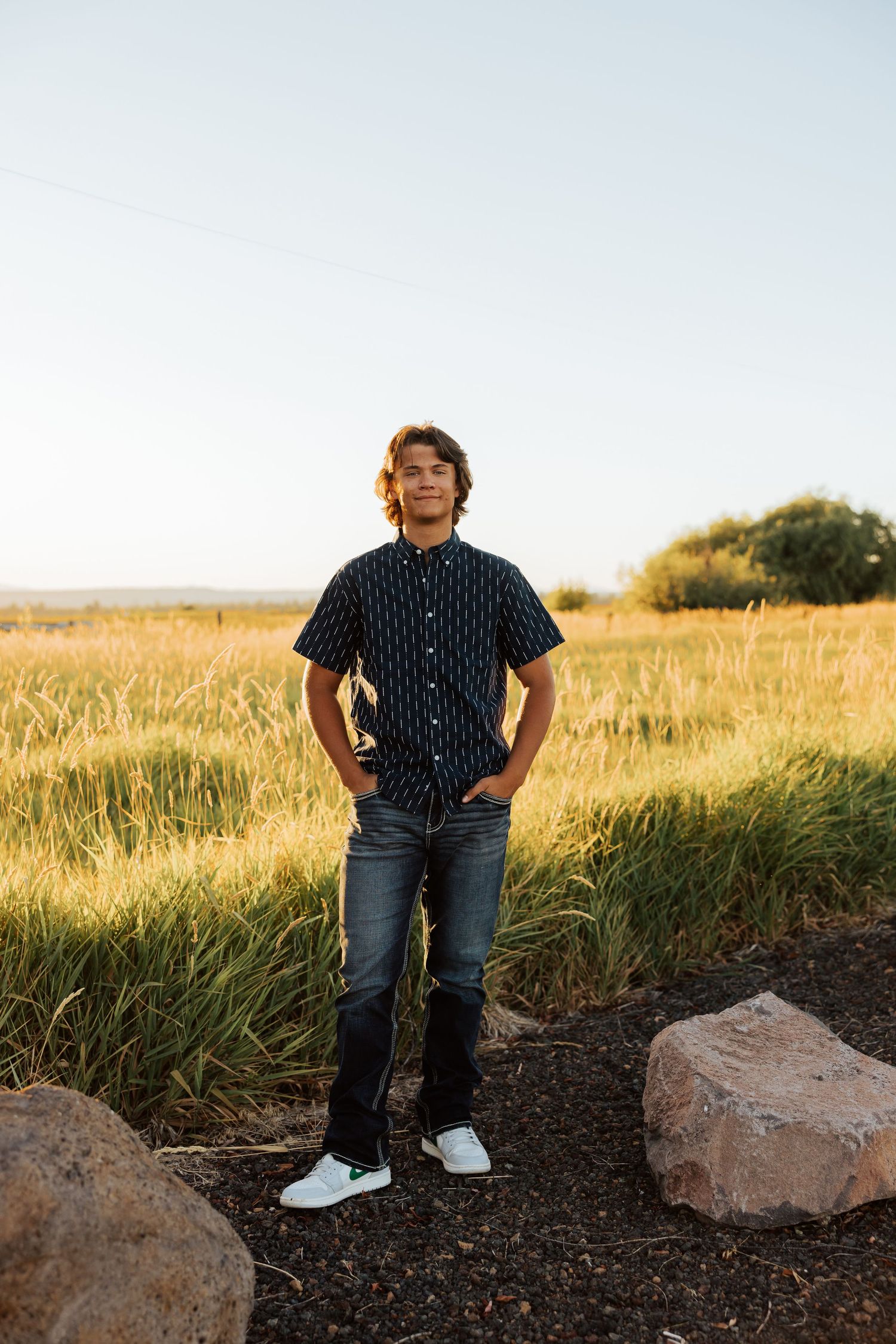 Someone poses near rocky terrain wearing a patterned shirt and jeans at golden hour.