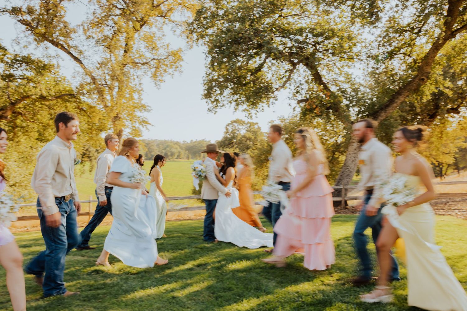 Festive wedding celebration with guests dancing on a grassy hillside under autumn trees.