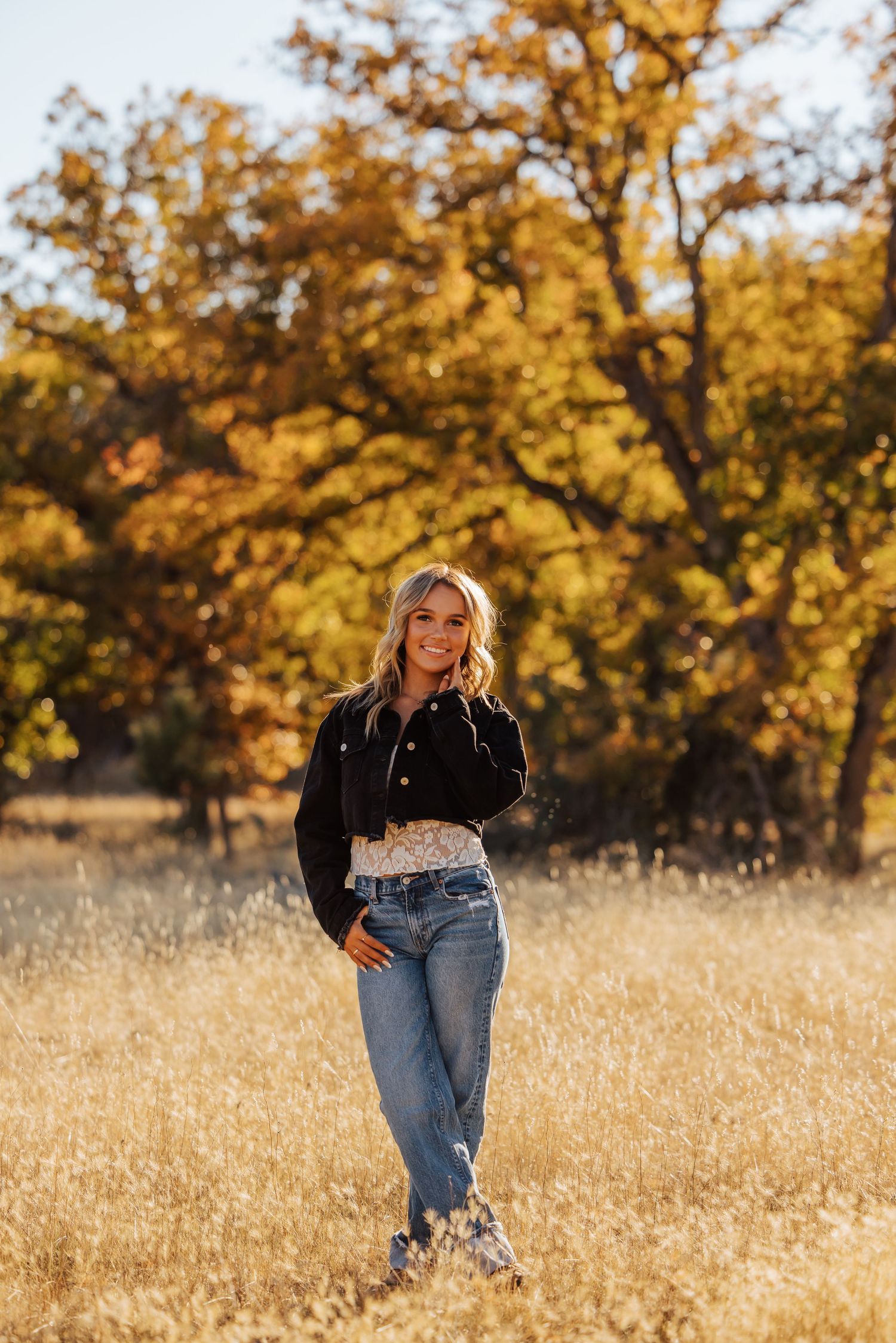Relaxed outdoor portrait in denim and black jacket against autumn foliage.