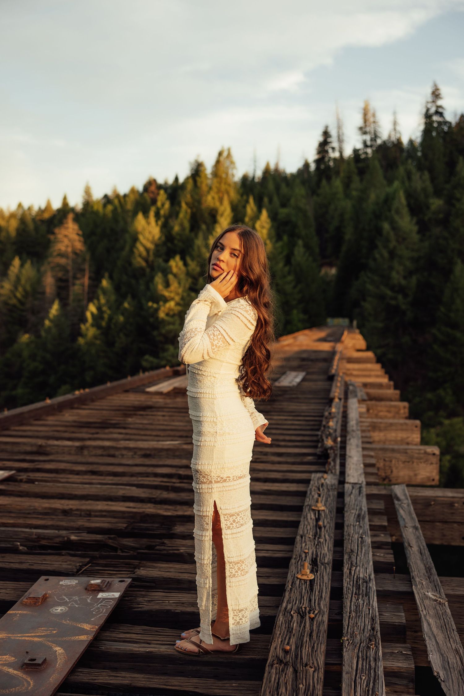 A person in white clothing stands on old wooden railroad tracks surrounded by evergreen forest.