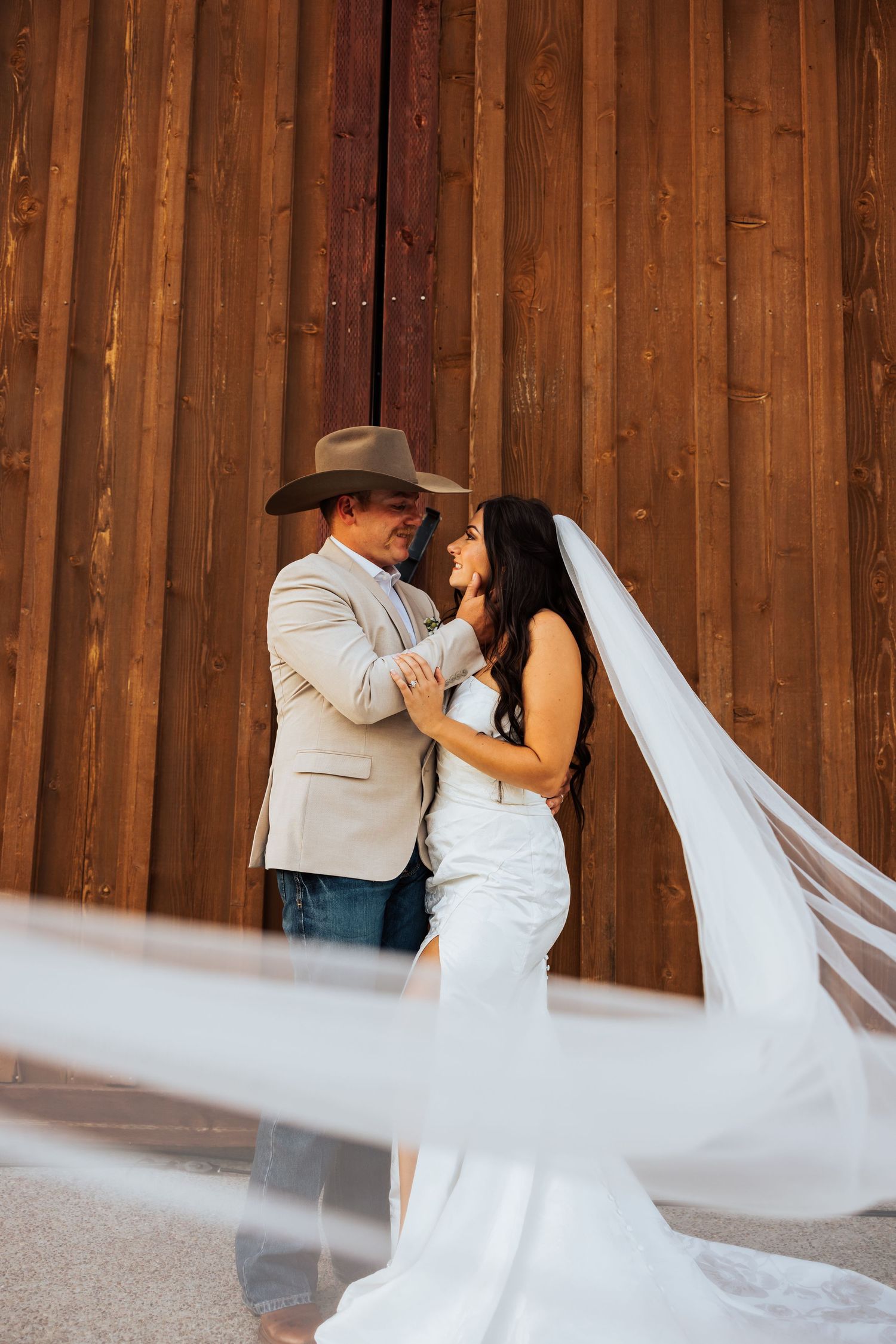Flowing white wedding veil creates dramatic movement during a romantic dance in a rustic barn setting.