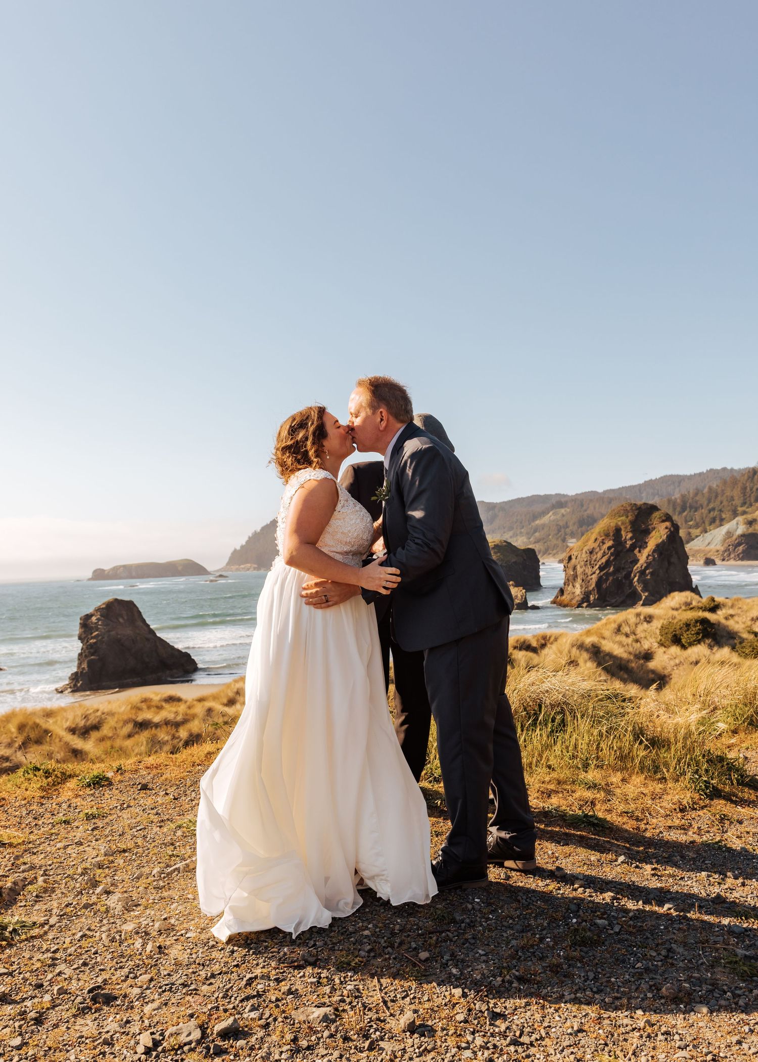 Newlyweds share an intimate moment on coastal cliffs surrounded by golden grass and ocean views.