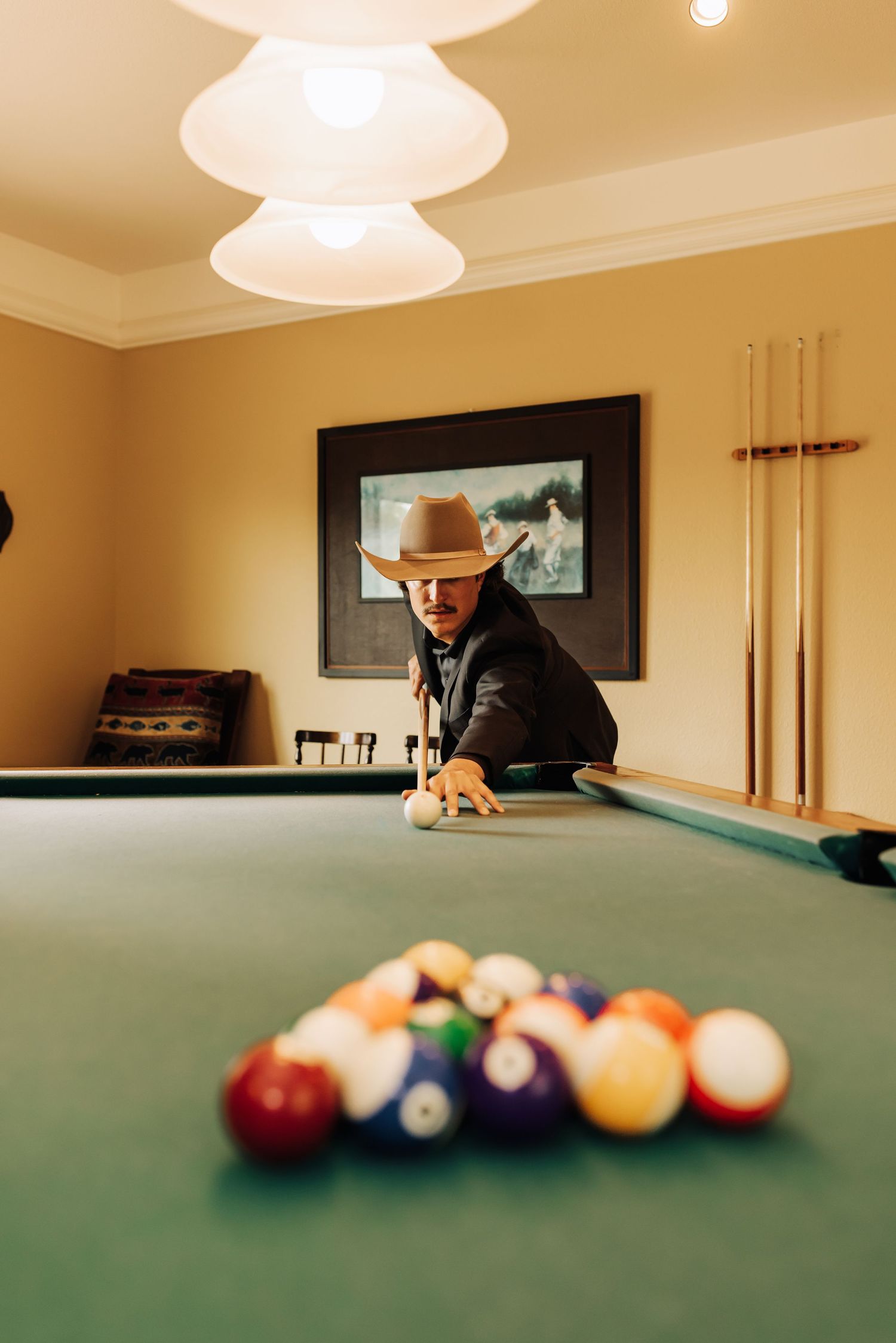 Person in cowboy hat playing pool with colorful billiard balls on green felt table.